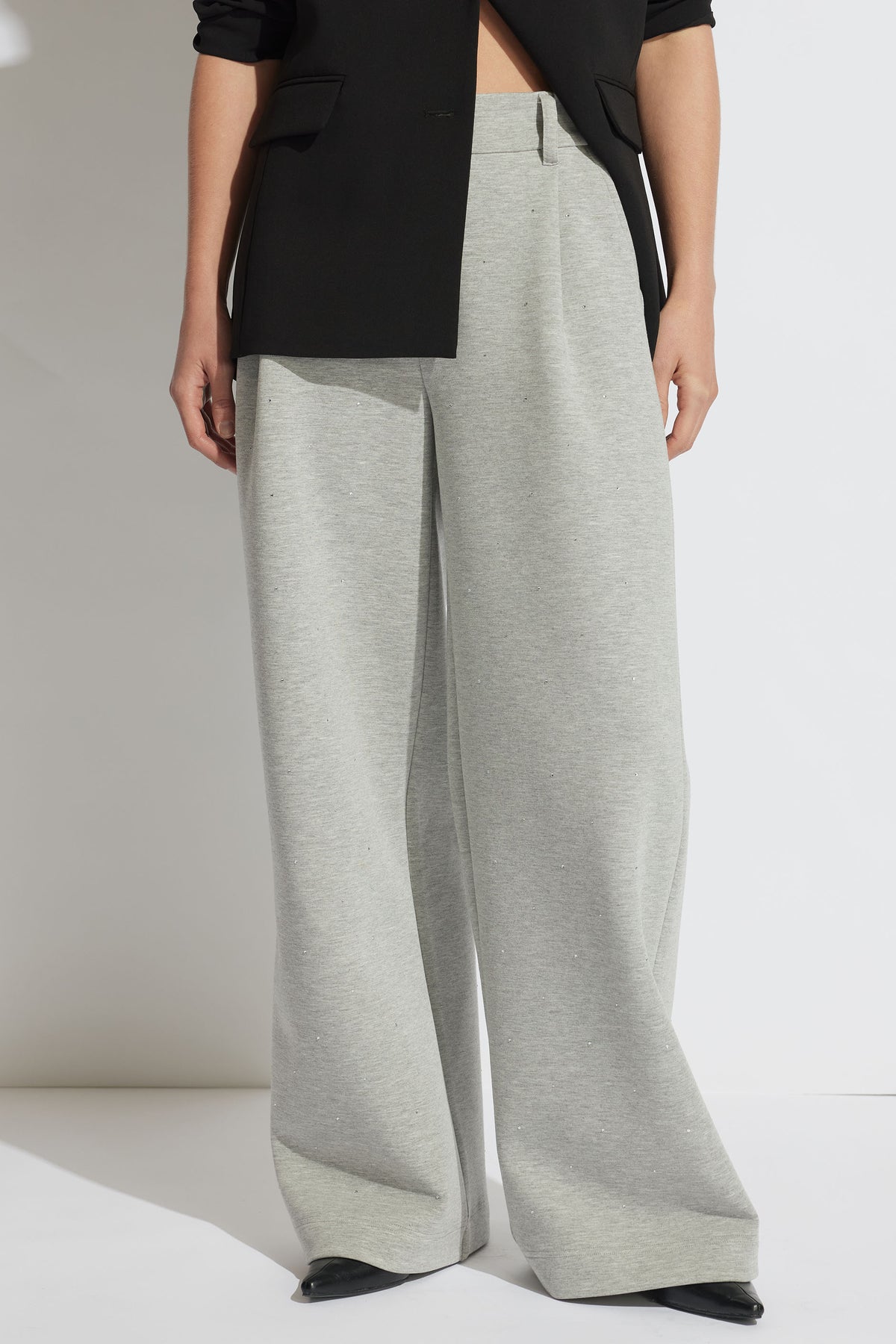 Front view of a woman wearing light grey wide-leg belted pull-on pants paired with a black blazer and shoes
