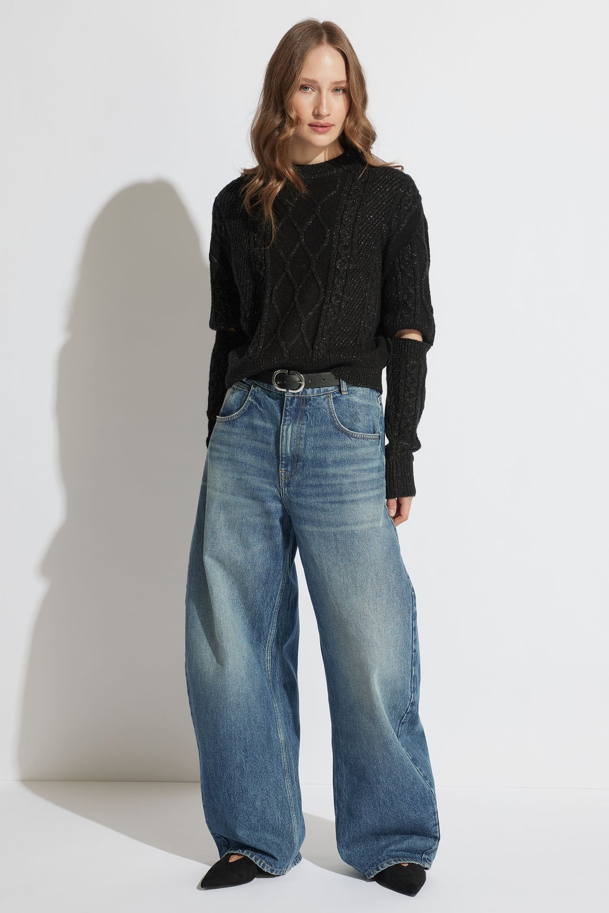 Model wearing Sasha Lurex Cable Knit Jumper with detachable sleeves styled with wide-leg denim jeans, gallery position one.
