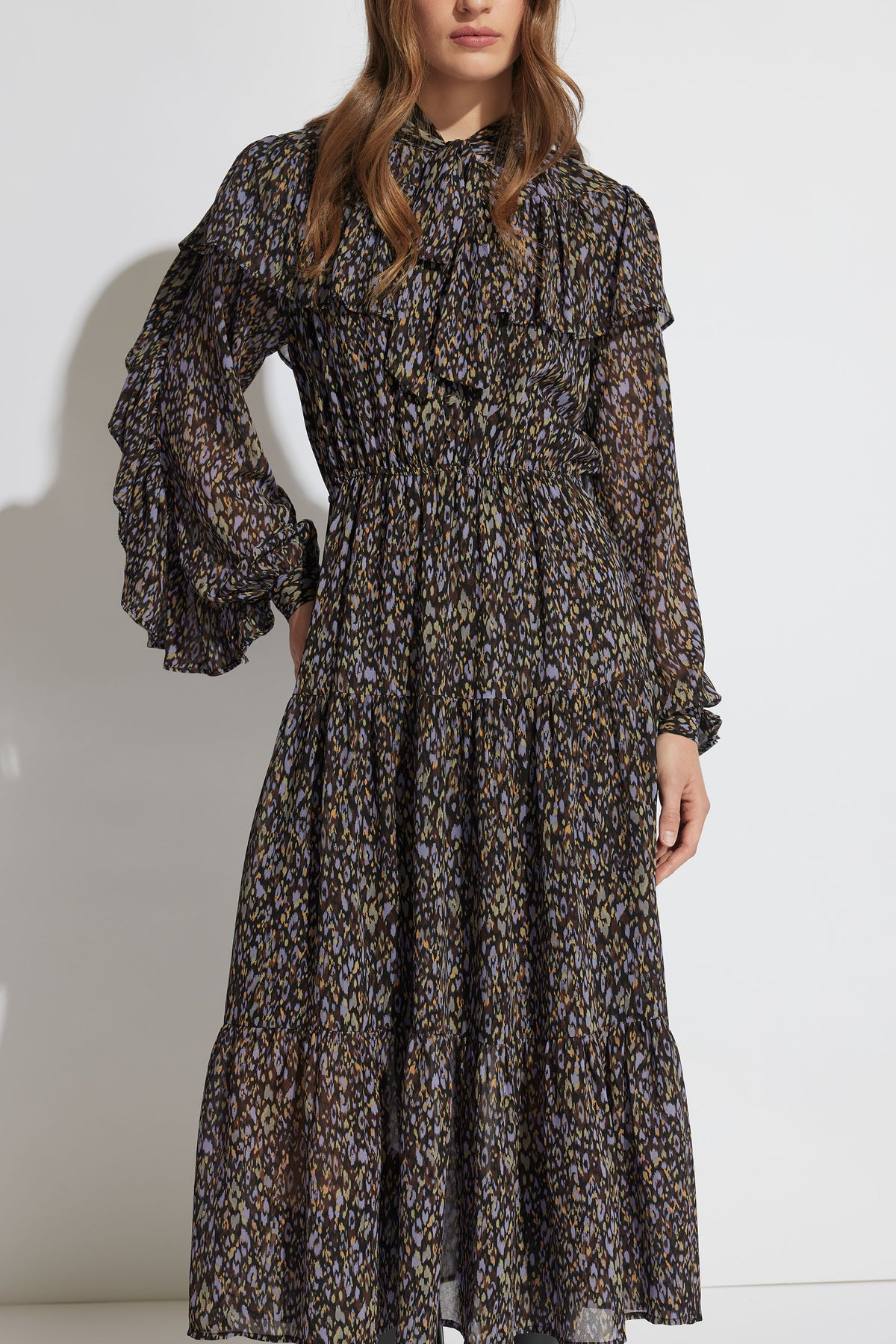 Woman wearing a tiered midi dress with ruffle details, long sleeves, and a subtle abstract pattern in muted tones.
