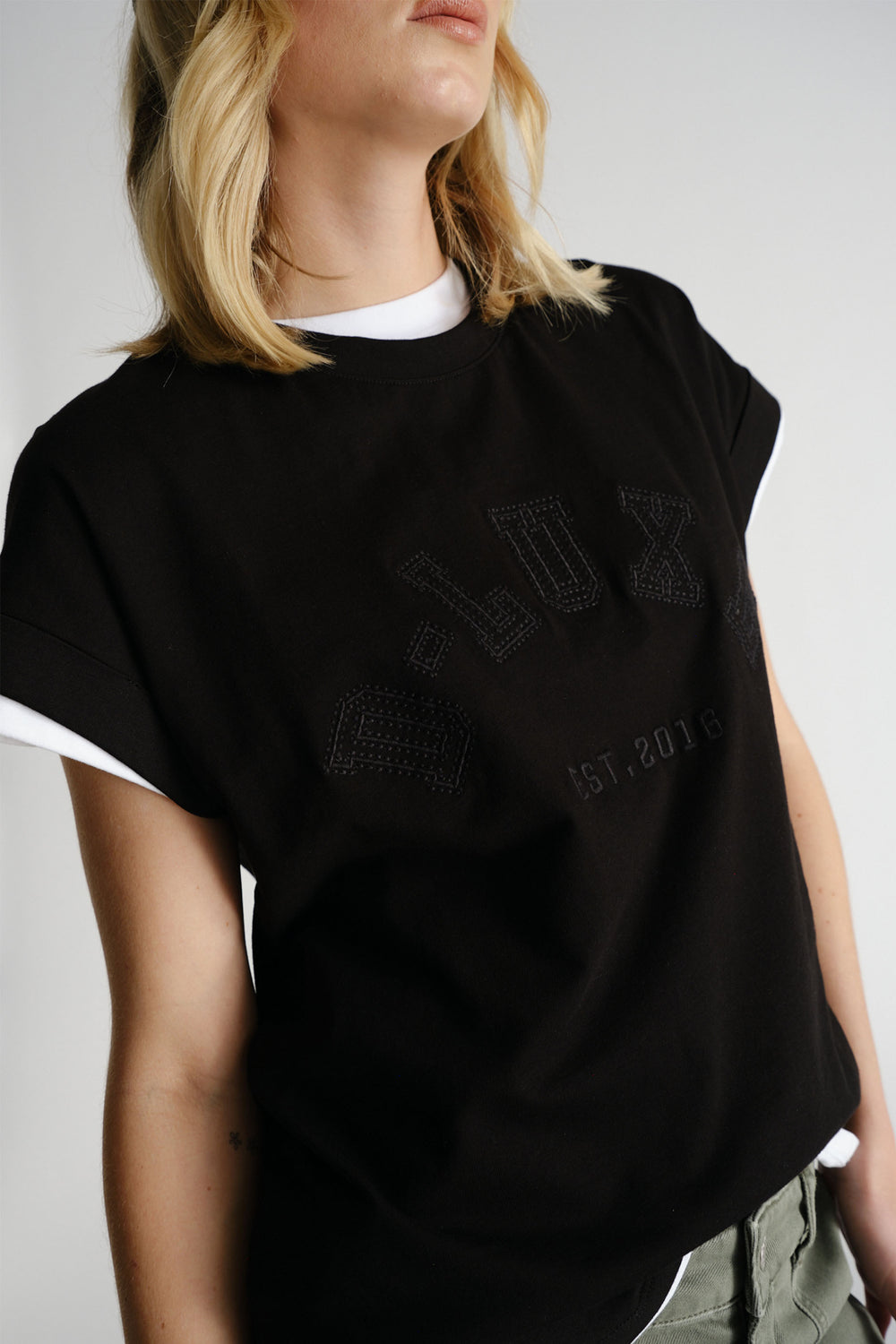 Woman wearing black D-Luxe Collegiate Tonal Tee layered over white top with casual olive pants by Decjuba Australian brand