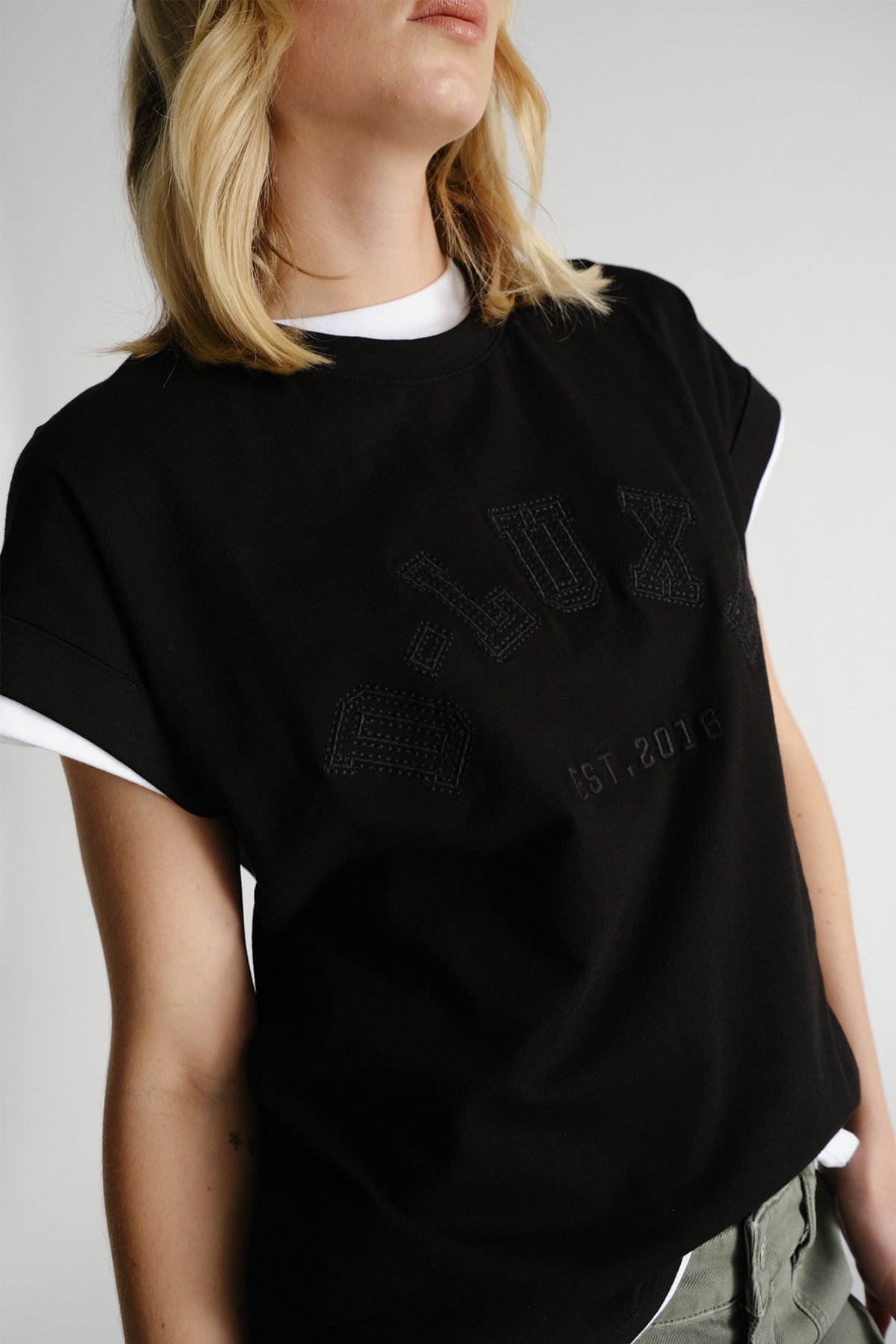 Woman wearing black D-Luxe Collegiate Tonal Tee layered over white top with casual olive pants by Decjuba Australian brand