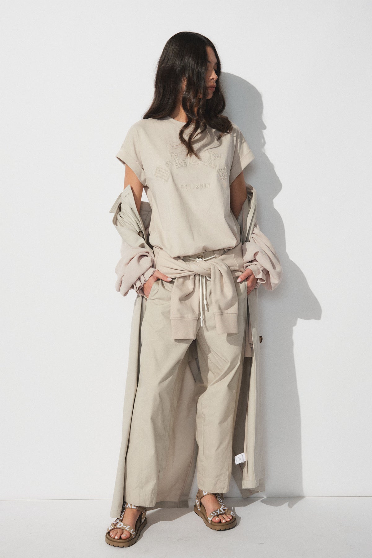 Woman in neutral-toned tee and wide-leg pants layered with a long coat and casual sandals for relaxed style.