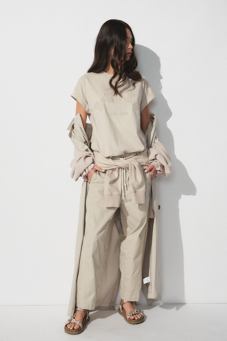 Woman in neutral-toned tee and wide-leg pants layered with a long coat and casual sandals for relaxed style.