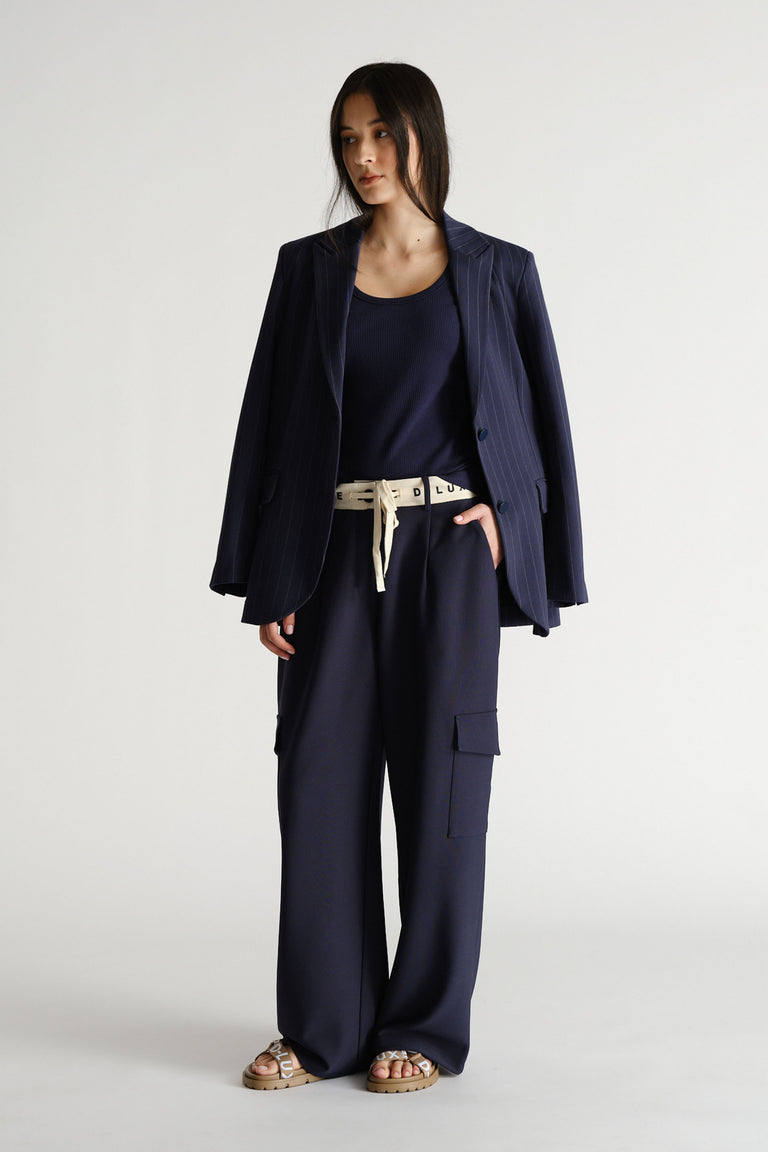 Woman wearing navy wide-leg pants with cargo pockets, a navy tank top, a pinstripe blazer, and tan sandals