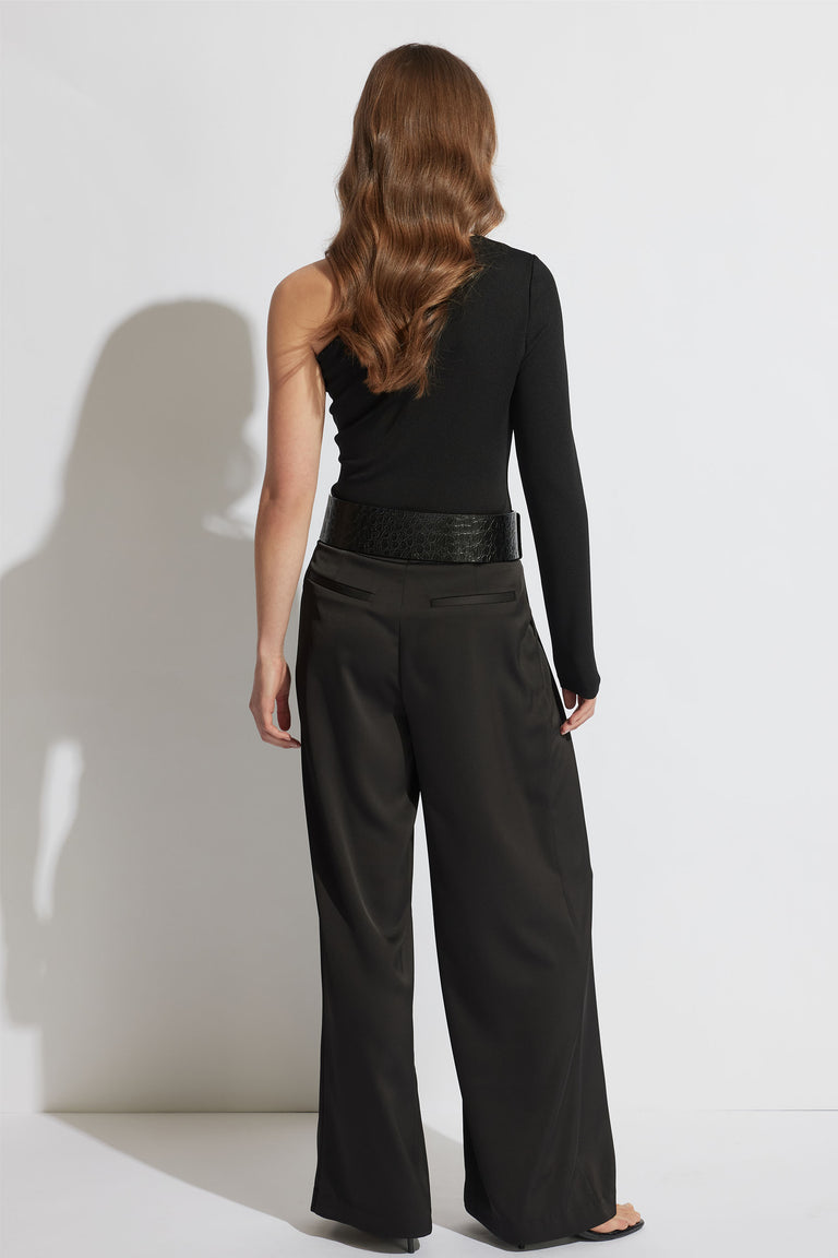 Woman wearing a black one-shoulder top with one long sleeve paired with wide-leg black trousers and a textured belt