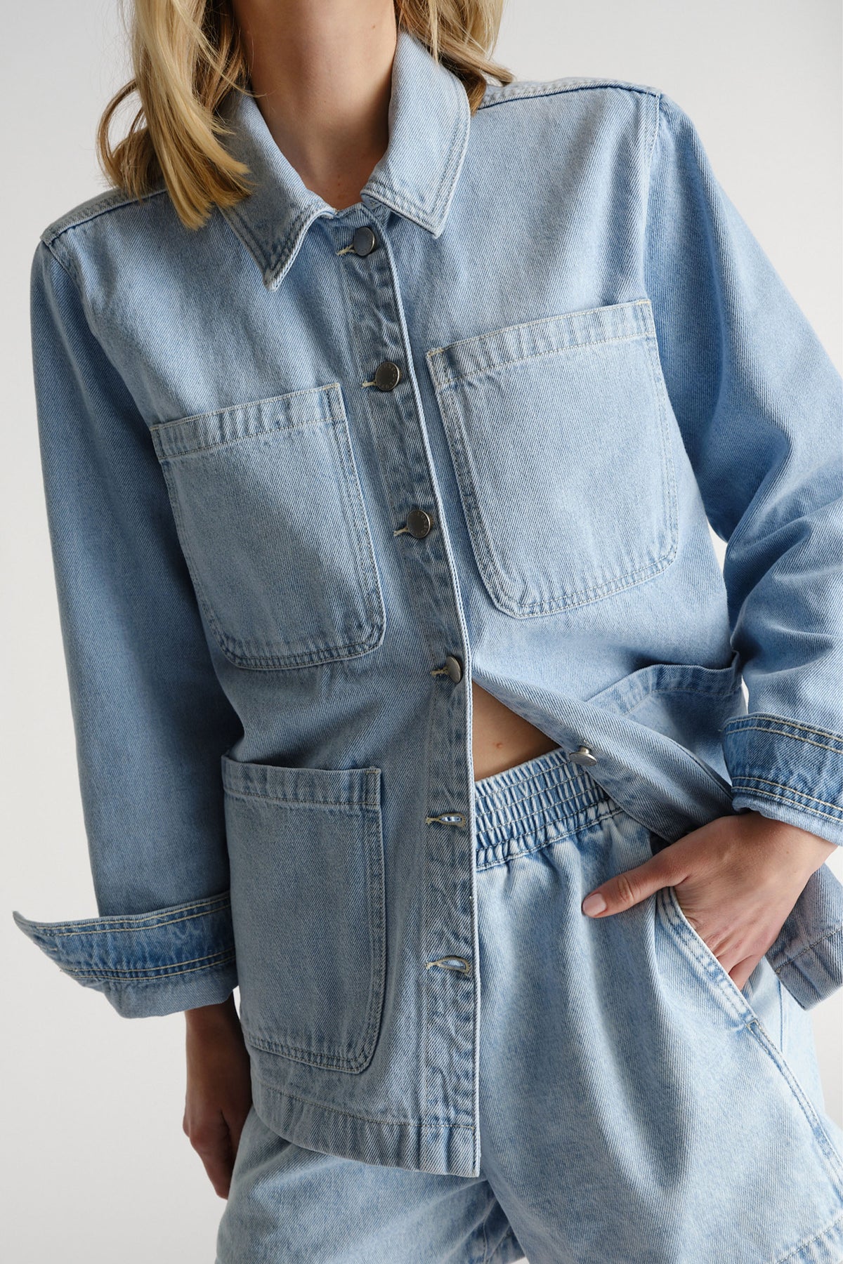 Light blue denim shacket with oversized patch pockets and relaxed sleeves paired with matching elastic waist pants.
