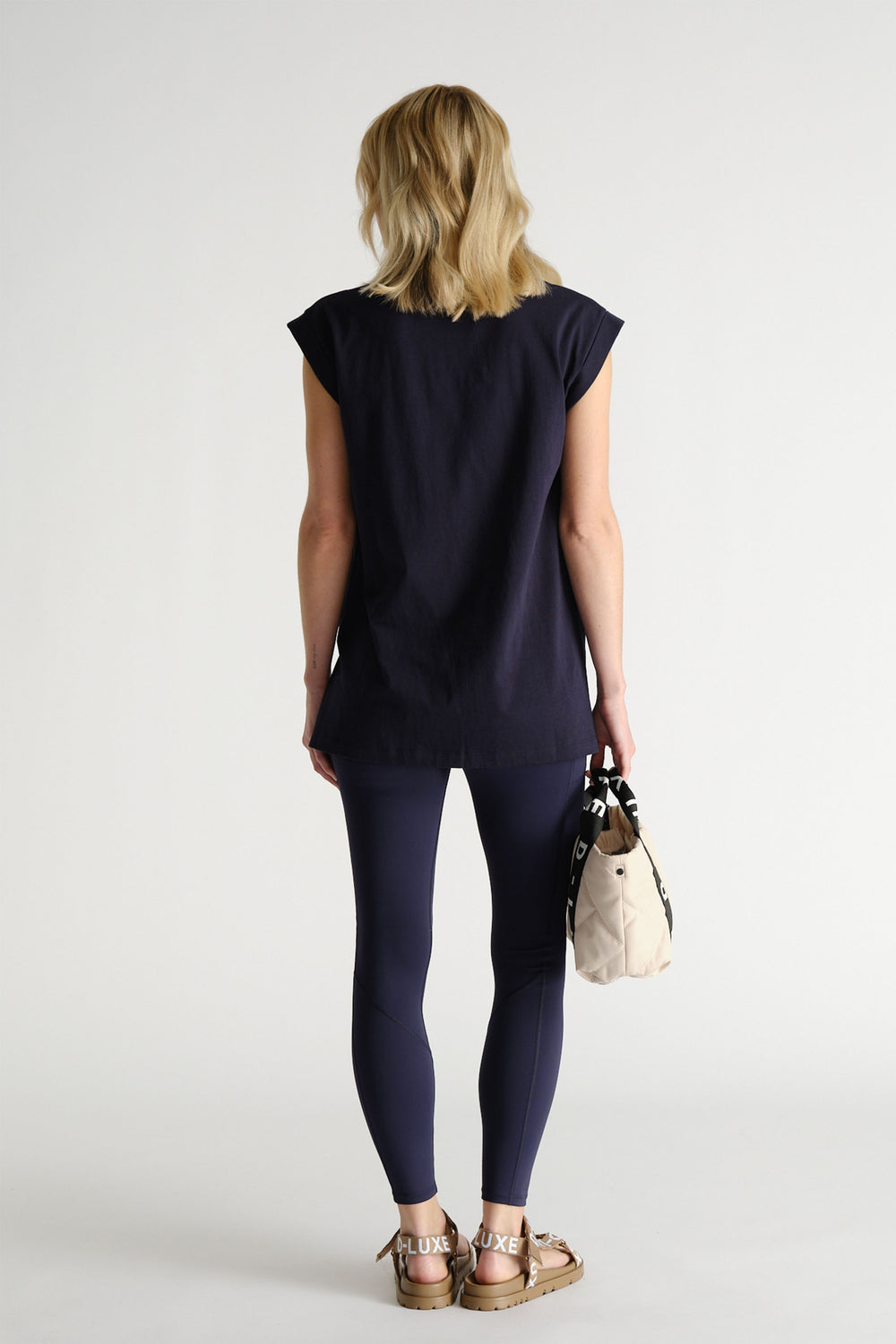 Back view of woman wearing a relaxed navy tank paired with fitted leggings and carrying a small beige bag