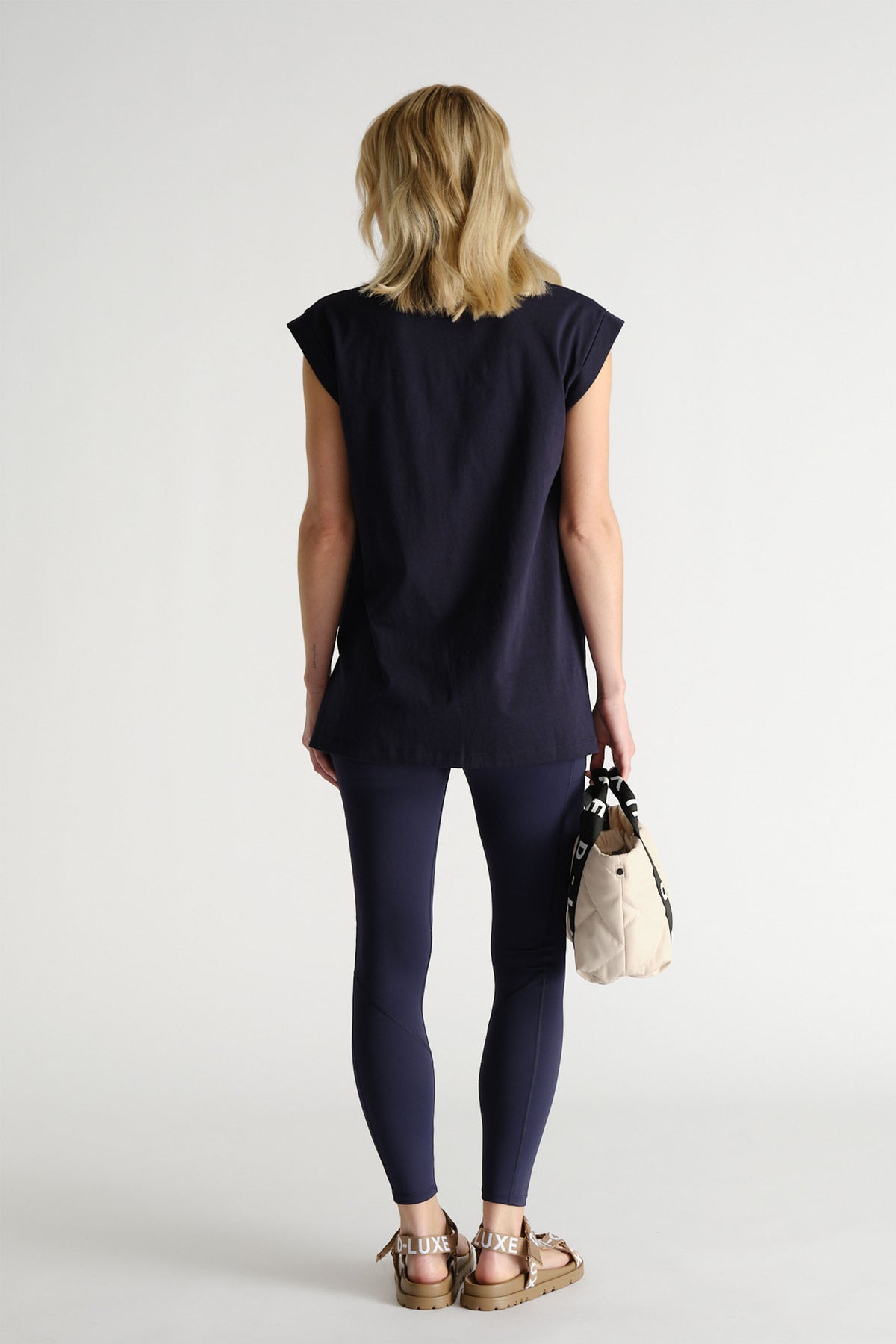 Back view of woman wearing a relaxed navy tank paired with fitted leggings and carrying a small beige bag