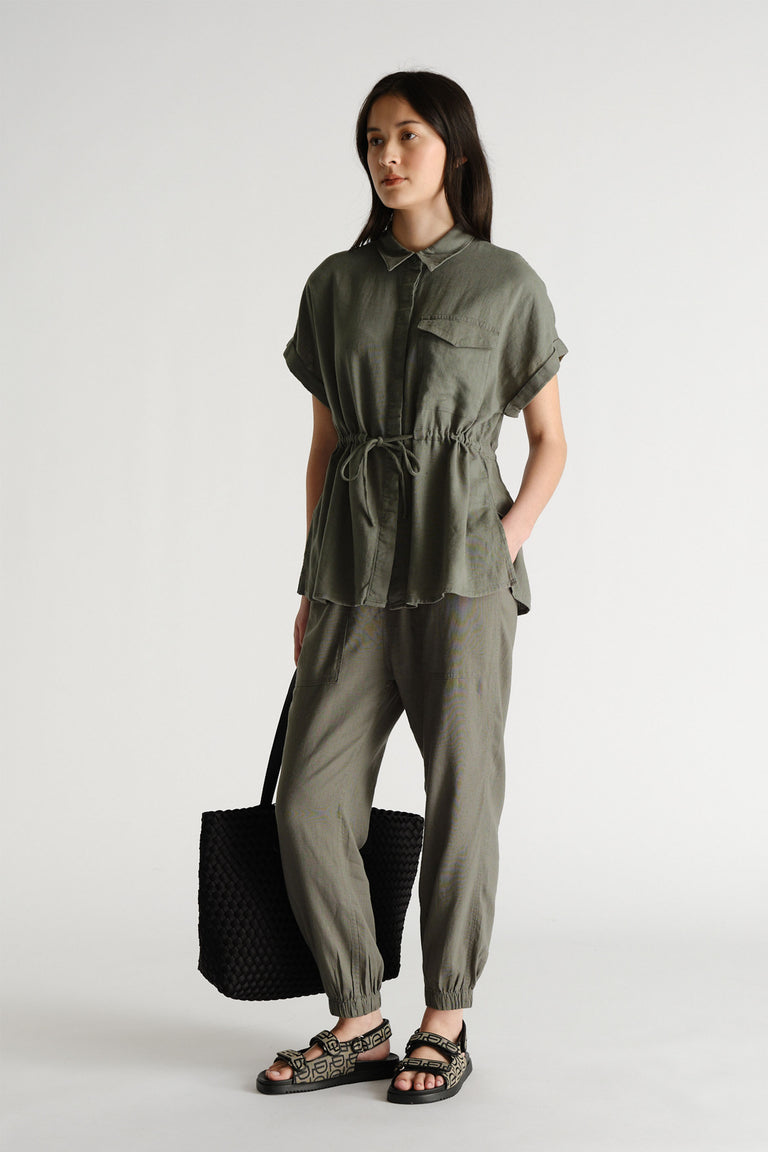Woman wearing a relaxed-fit olive linen blend top with drawstring waist and matching jogger pants paired with black sandals and a tote bag