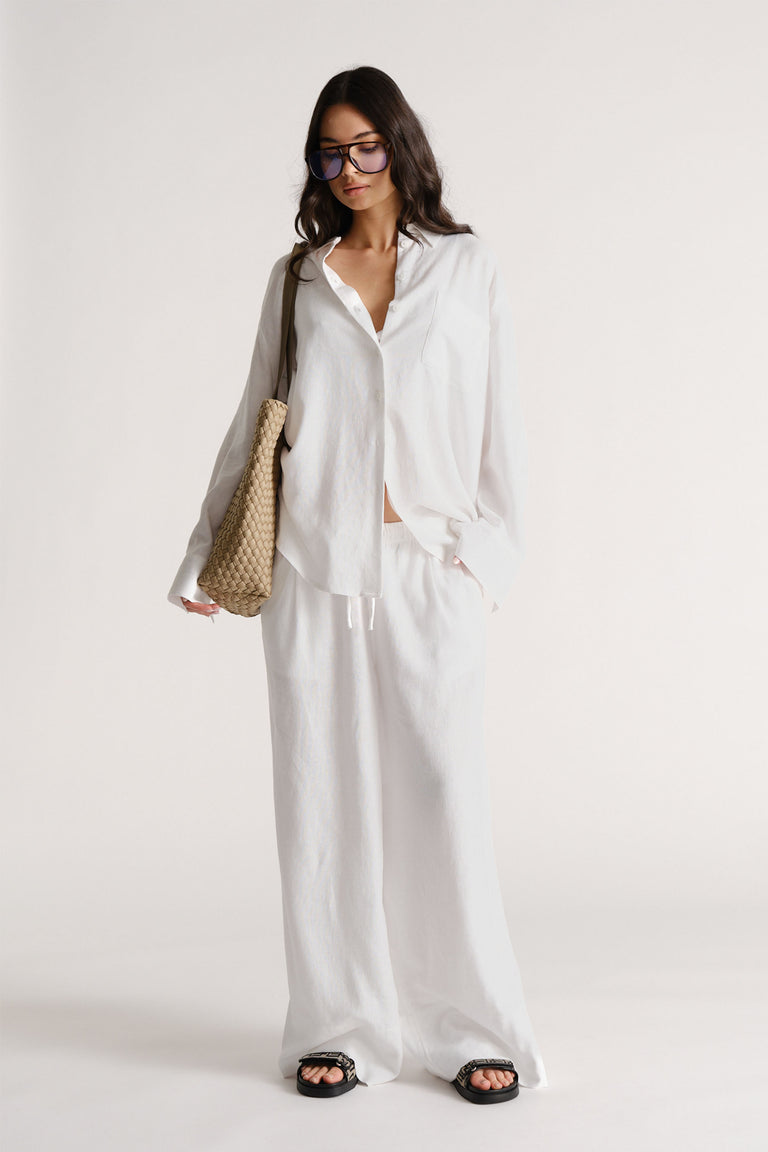 Woman wearing D-Luxe Linen Blend Pant in portrait view, styled with loose white shirt and woven bag, gallery image 1