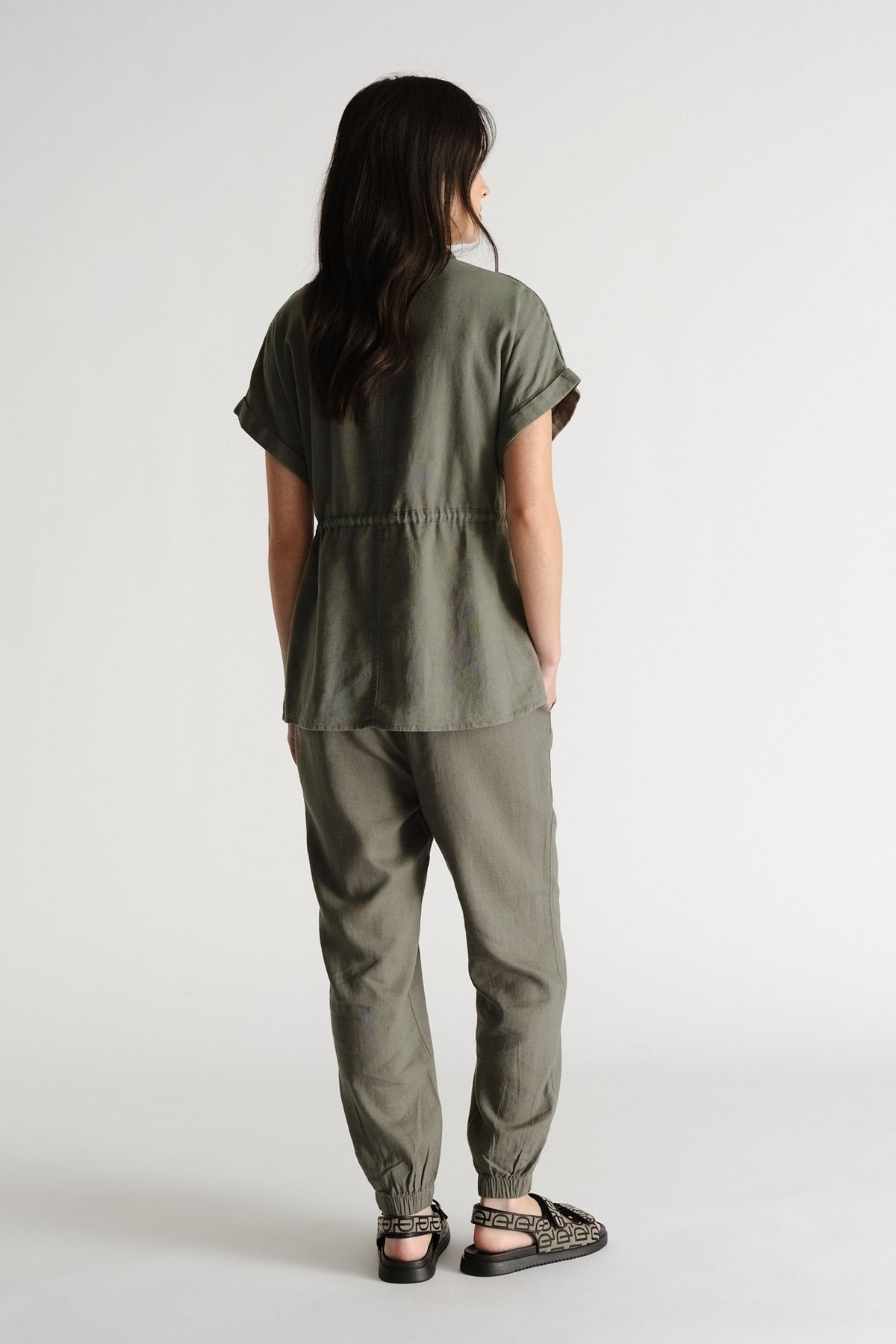 Woman seen from behind wearing relaxed-fit thyme green linen blend joggers paired with a matching short-sleeve top