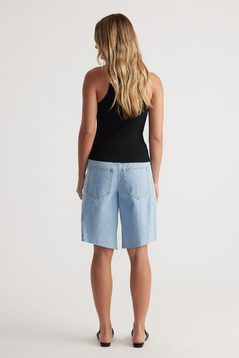 Back view of a woman wearing a black racer back knit tank paired with relaxed light-wash denim bermuda shorts.