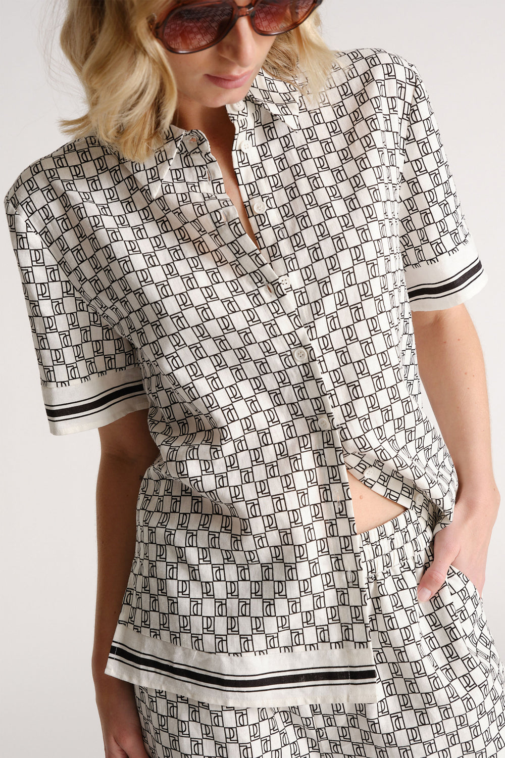 Woman wearing a patterned short sleeve button-up shirt and matching shorts with black trim detail, styled casually.