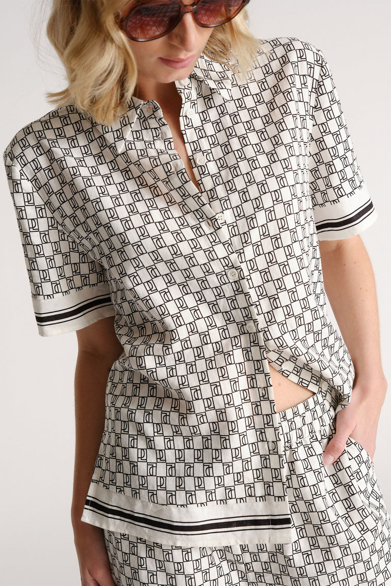 Woman wearing a patterned short sleeve button-up shirt and matching shorts with black trim detail, styled casually.