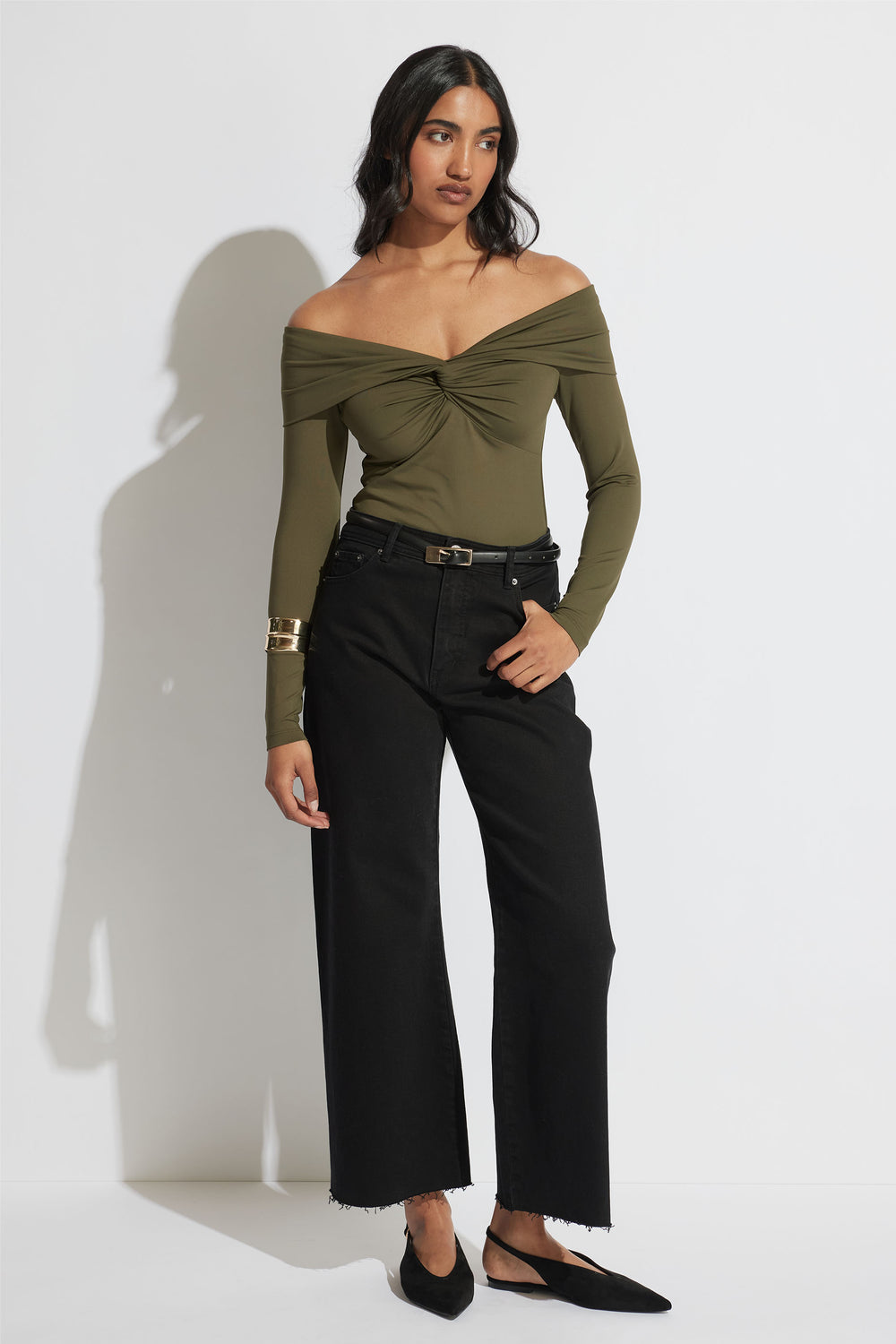 Woman wearing an olive twisted off-shoulder long sleeve top paired with black wide-leg cropped jeans and black flats