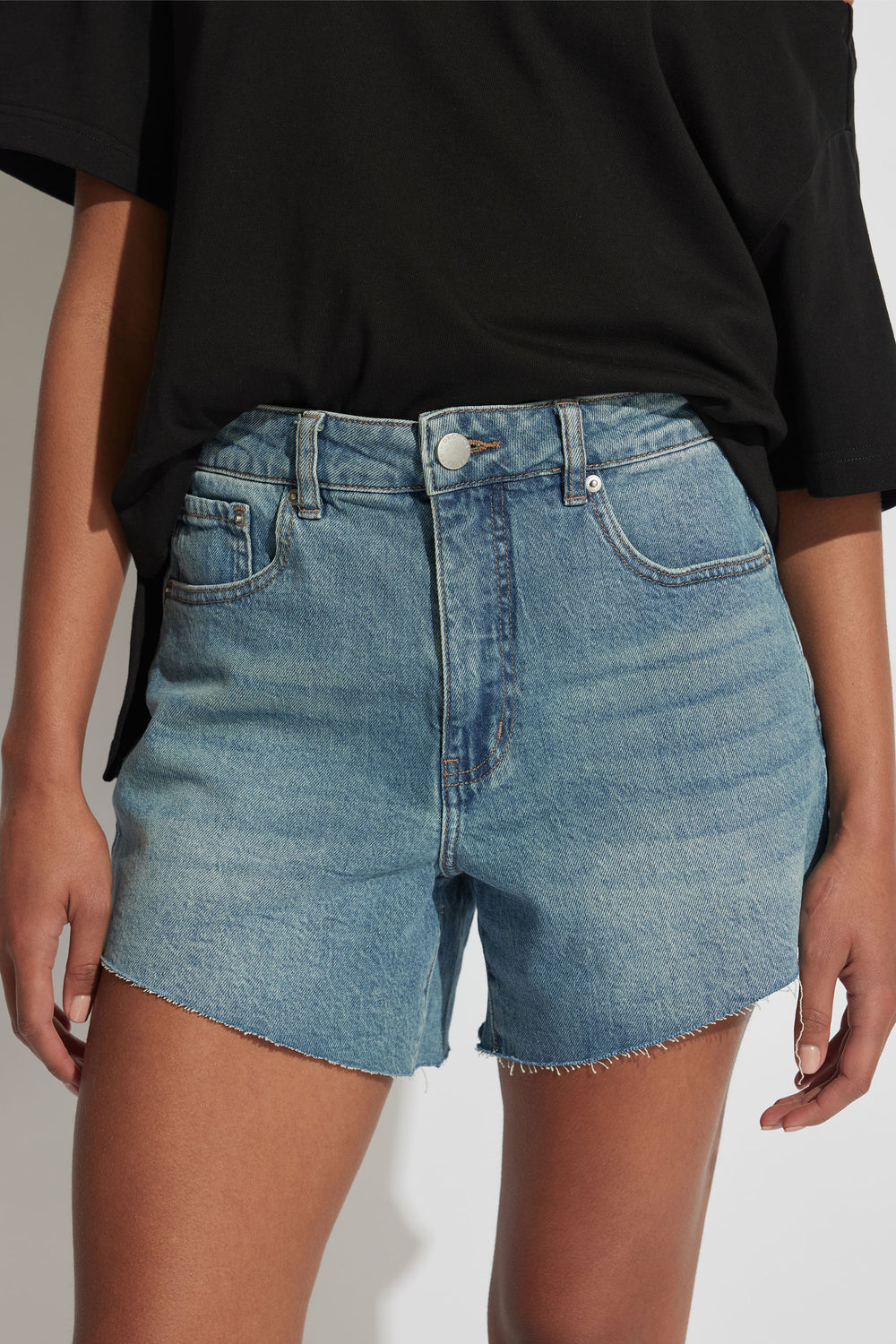 Woman wearing faded blue high-rise denim shorts with raw hem paired with a loose black tee, cropped view.