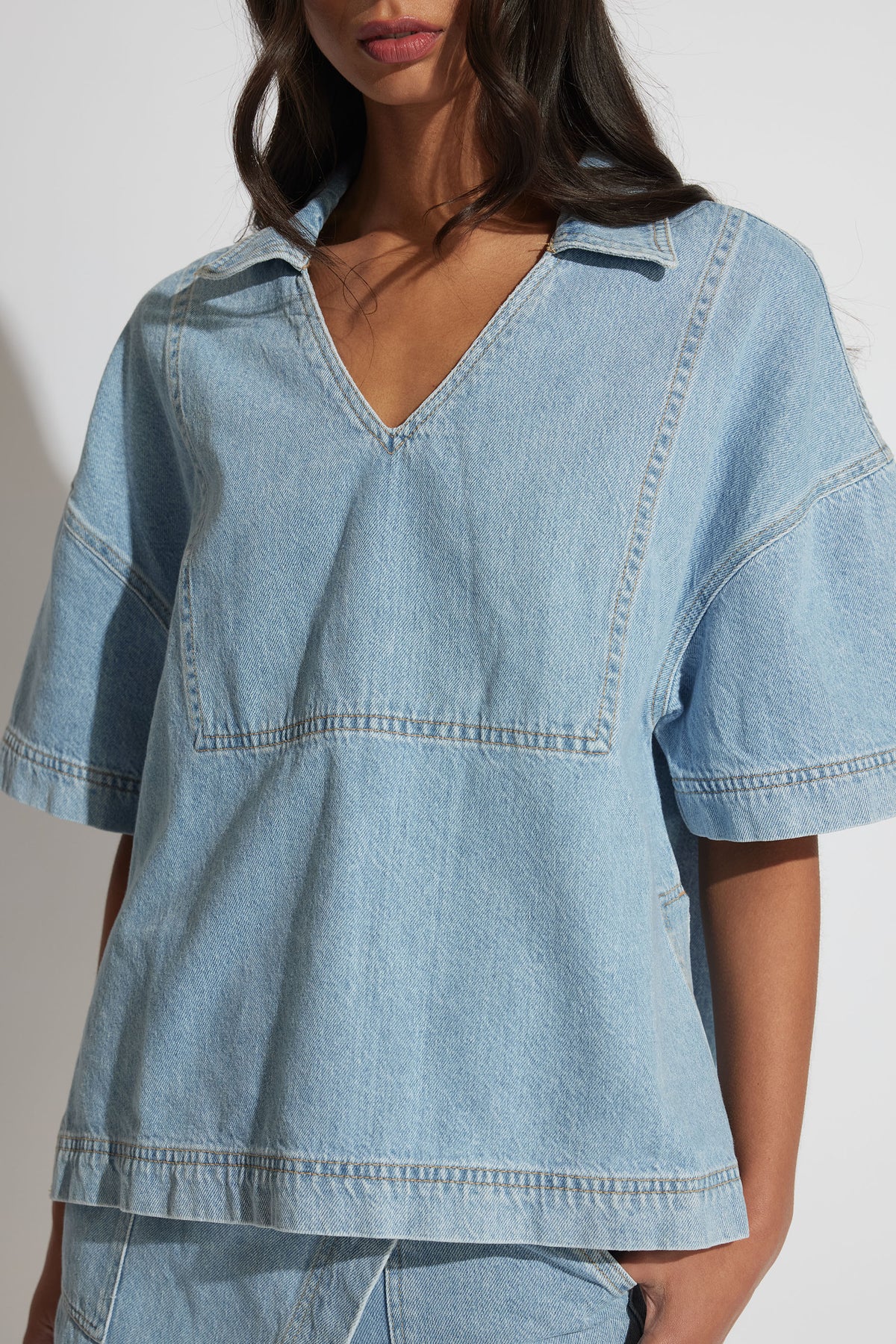 Woman wearing a light washed oversized denim shirt with a deep V neckline and short sleeves in soft structured fabric