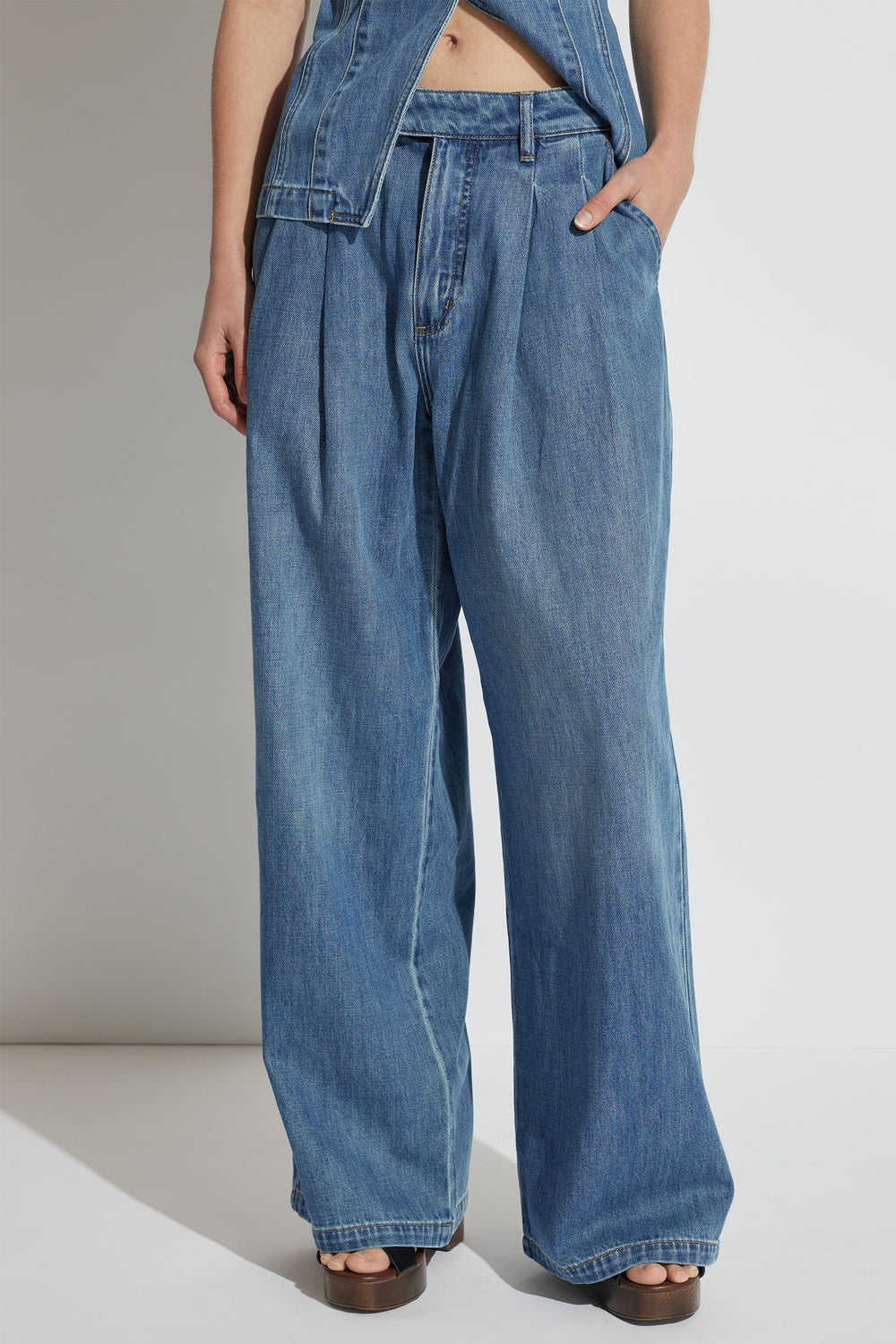 Wide-leg blue denim jeans with pleated front detail styled with open-toe brown sandals and a matching denim jacket