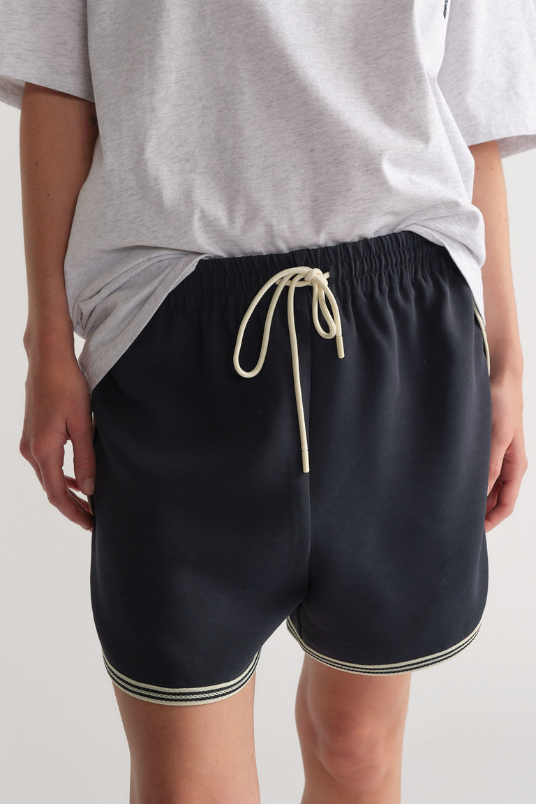 Front view of navy racer stripe shorts with elastic waist and drawstring paired with a relaxed light grey tee