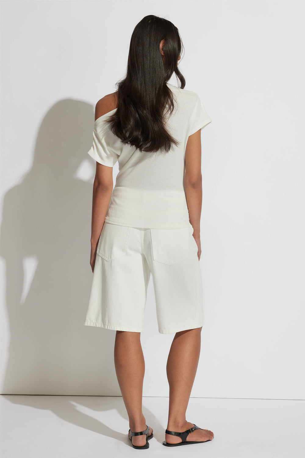 Woman wearing an ivory gathered top with short sleeves and relaxed white knee-length shorts paired with black sandals.