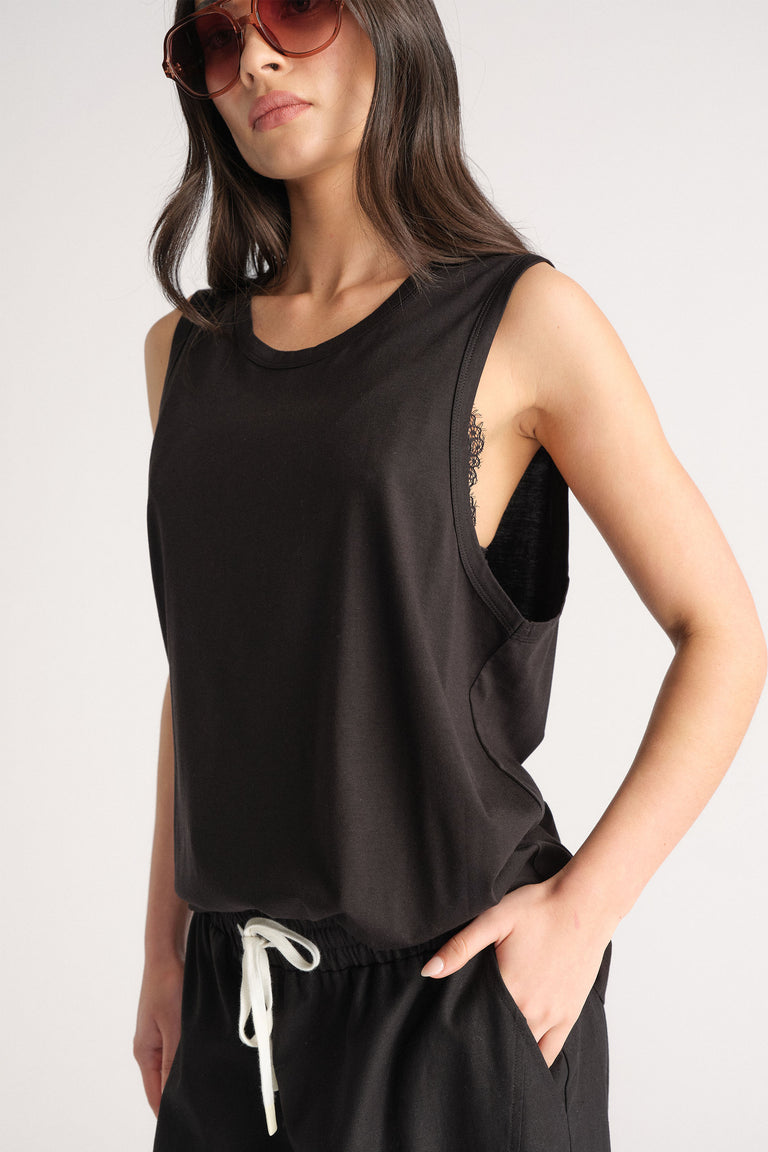 Woman wearing a relaxed black sleeveless tank with wide armholes styled with casual black drawstring pants and sunglasses