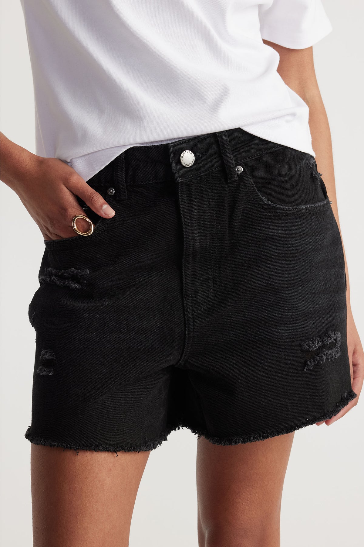 Close-up of black distressed denim shorts with frayed hems styled with a casual white top and gold ring accessory.