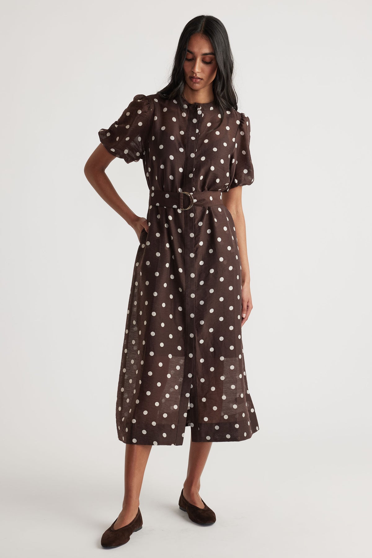 Woman wearing Becca Puff Sleeve Midi Dress in brown with white polka dots, belt, and button through closure, gallery position 1.