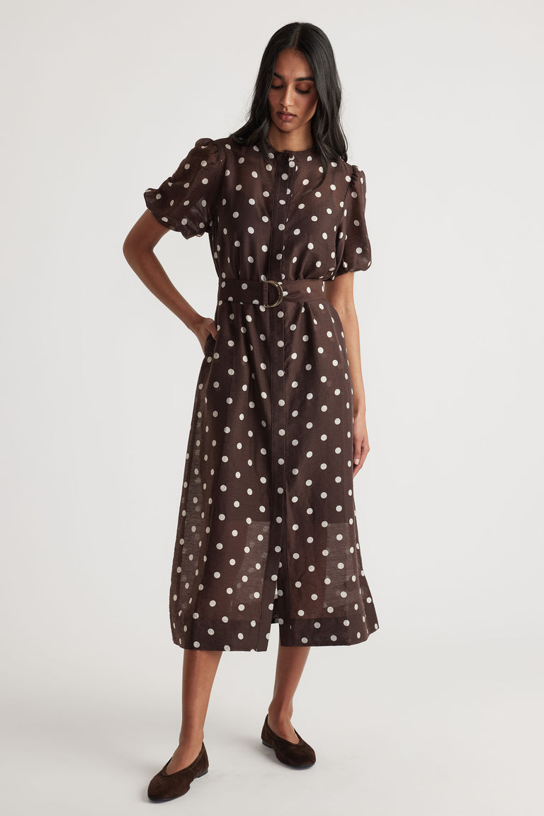 Woman wearing Becca Puff Sleeve Midi Dress in brown with white polka dots, belt, and button through closure, gallery position 1.