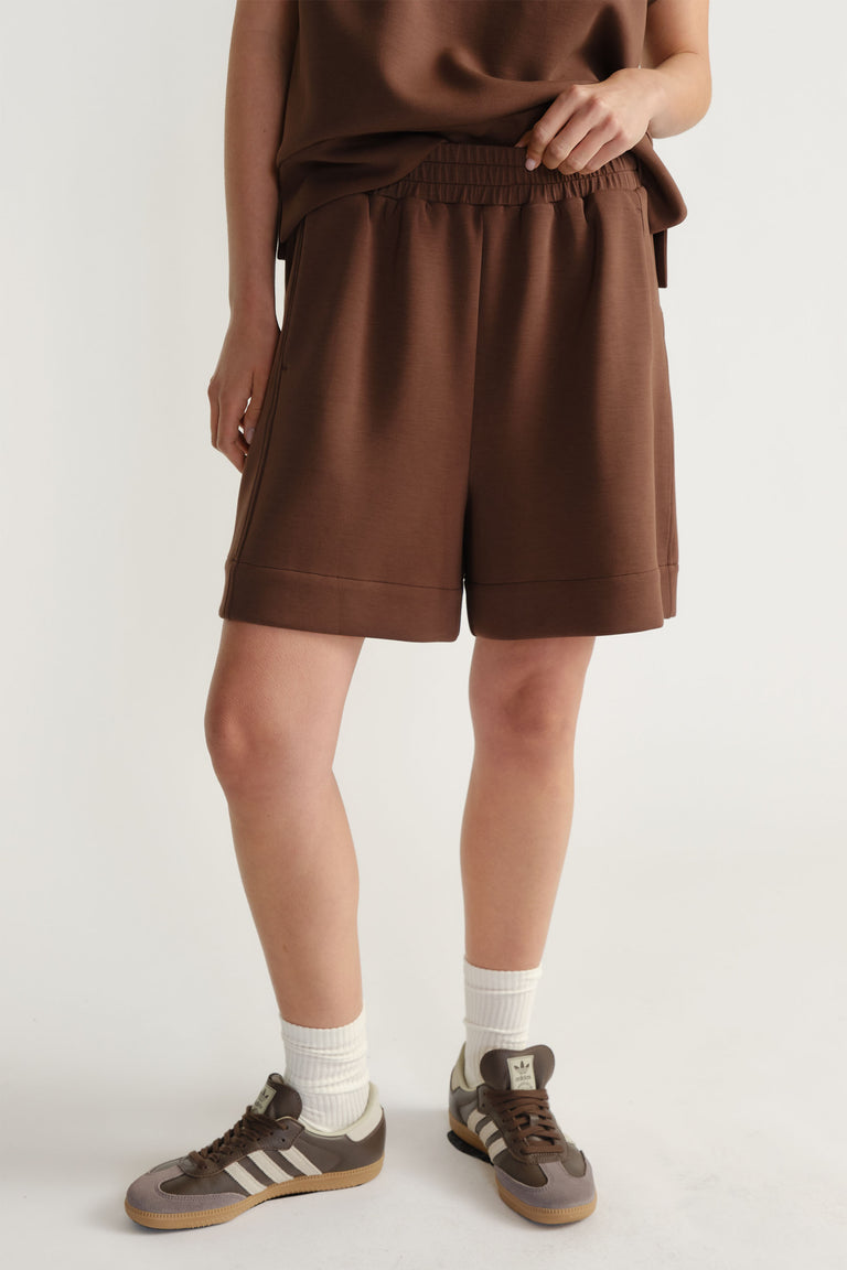 Woman wearing relaxed-fit brown neoprene shorts with elastic waistband paired with casual sneakers and white socks