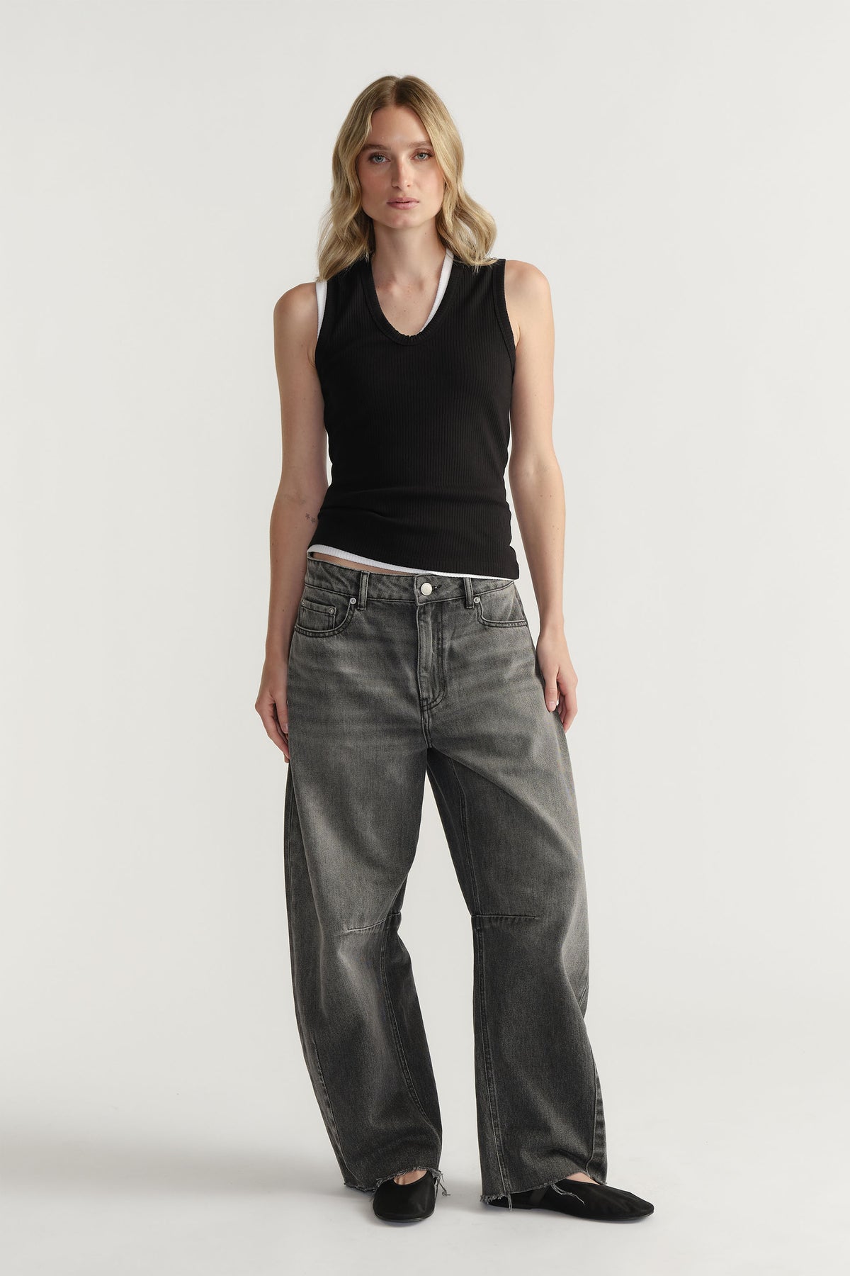 Woman wearing a fitted black ribbed tank top paired with loose-fit faded grey jeans and black flat shoes.