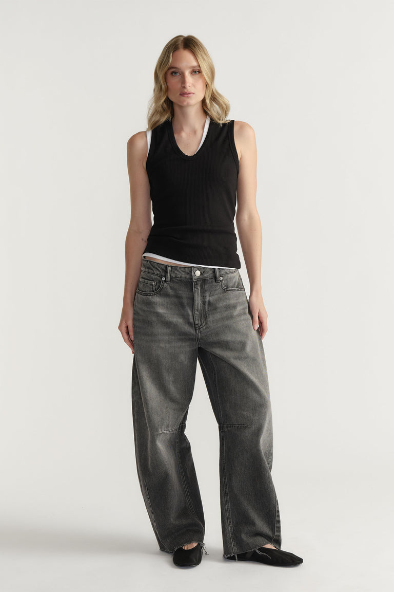 Woman wearing a fitted black ribbed tank top paired with loose-fit faded grey jeans and black flat shoes.