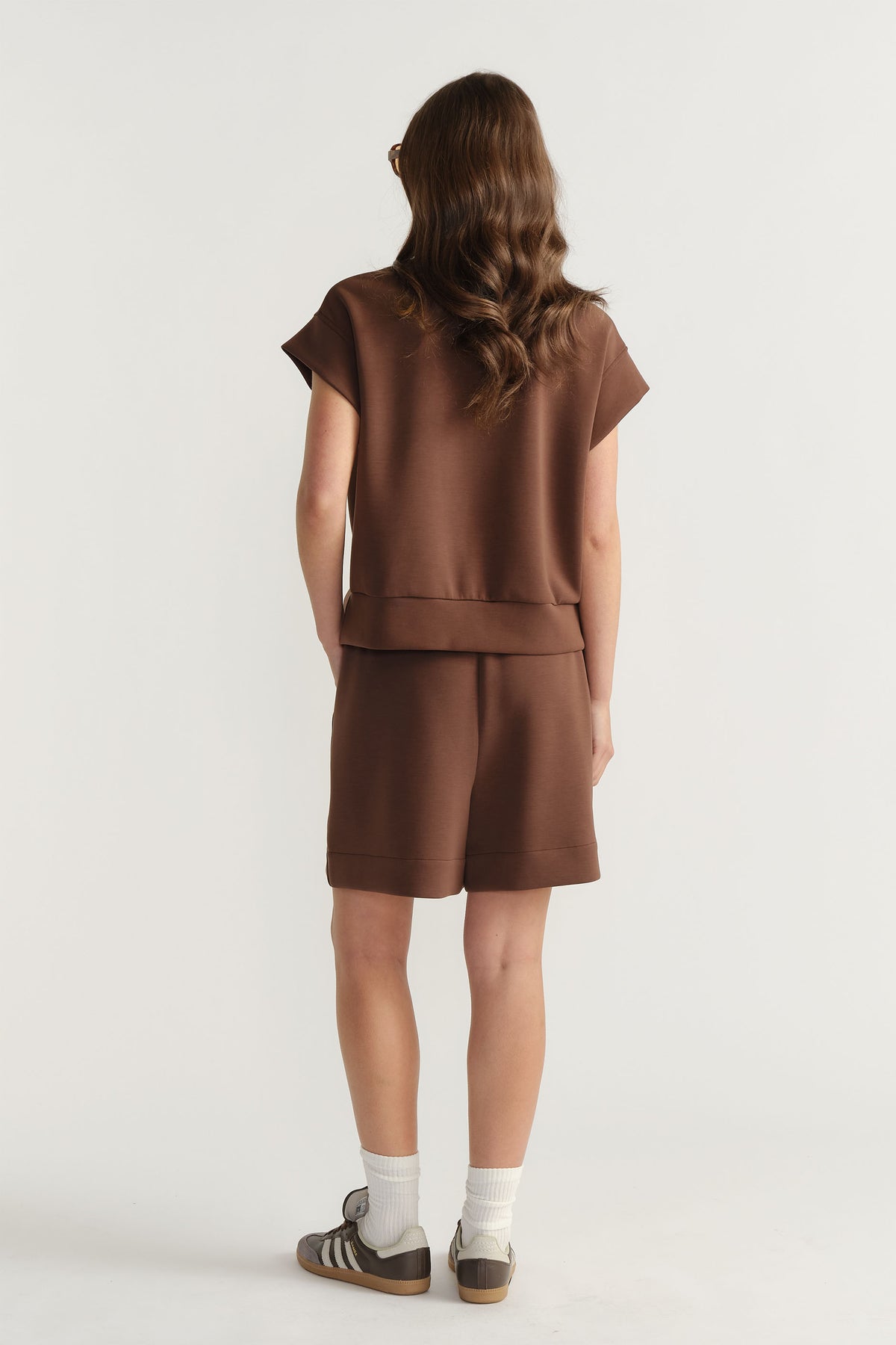 Back view of woman wearing a relaxed-fit brown neoprene half zip top and matching shorts for casual style