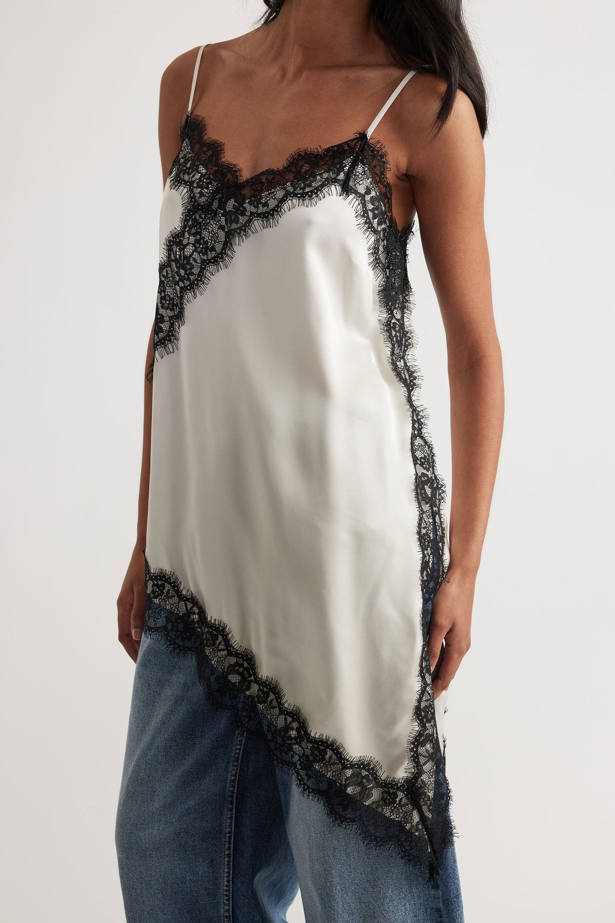 Karla Lace Tunic in portrait with thin straps, black lace trim, asymmetrical hem paired with blue denim jeans.