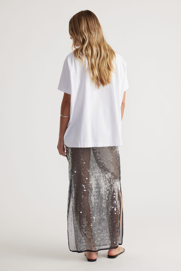 Woman wearing a white t-shirt and Savannah Sequin Skirt with side splits, elastic waist, and semi sheer maxi length back view.