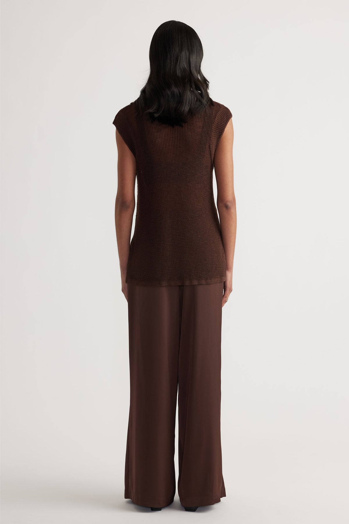Back view of woman wearing a sleeveless coffee brown knit tank paired with relaxed wide-leg trousers in matching tones