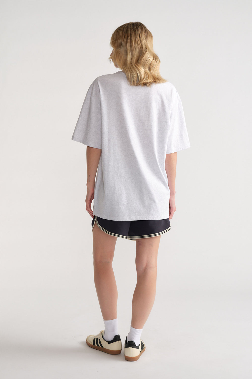 Back view of woman wearing a relaxed light grey tee paired with sporty black shorts and retro sneakers
