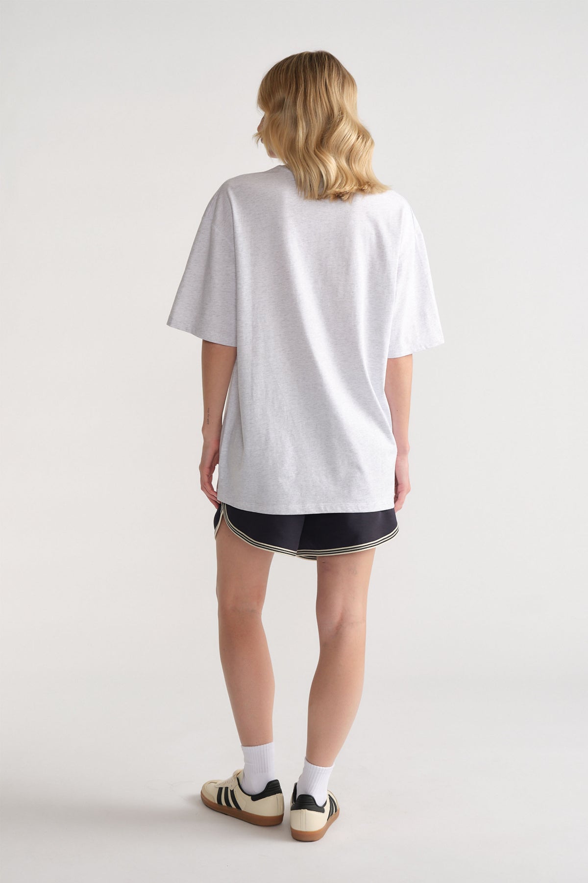 Back view of woman wearing a relaxed light grey tee paired with sporty black shorts and retro sneakers