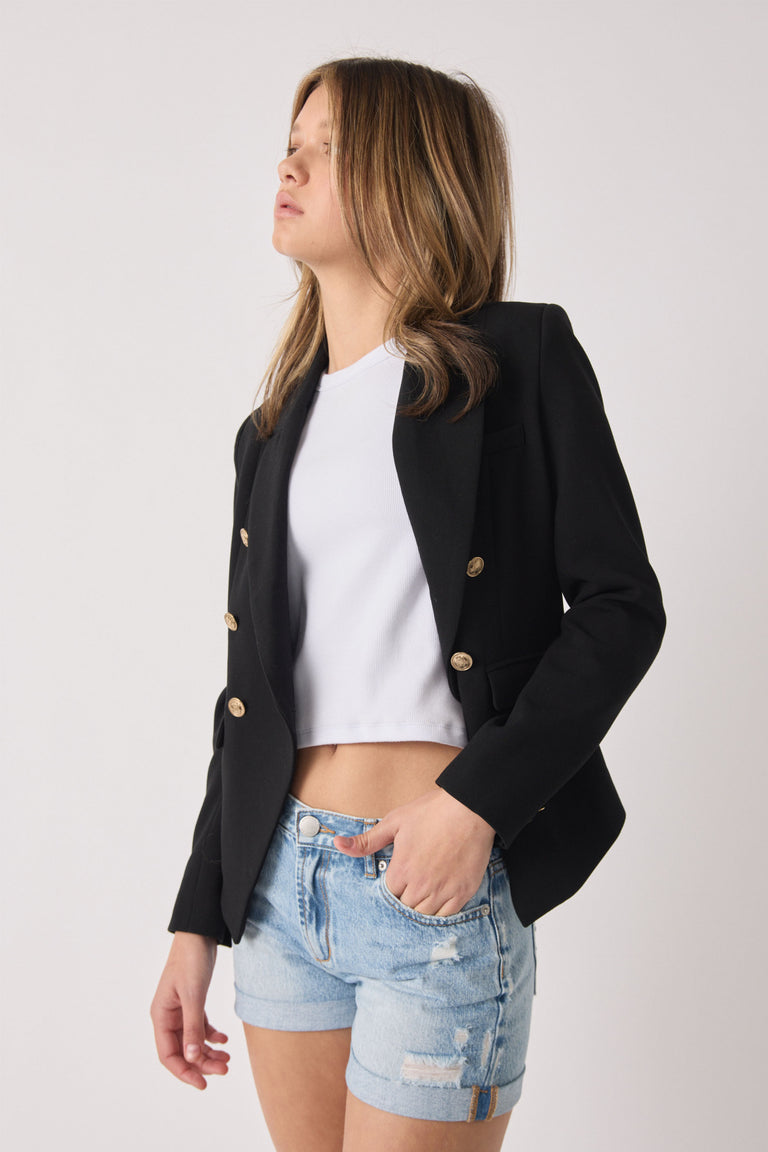 Teen girl wearing a tailored black button blazer over a white crop top with distressed light denim shorts for a casual look