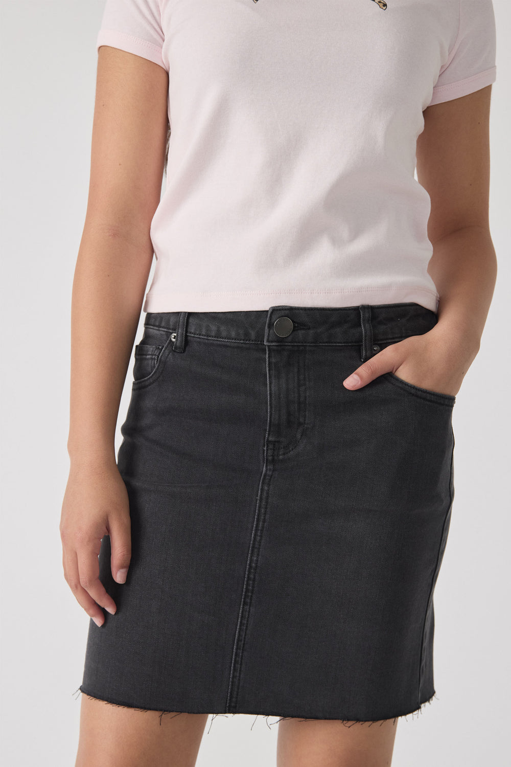 Girl wearing a washed black denim skirt with raw hem and classic five-pocket styling, paired with a light pink top.