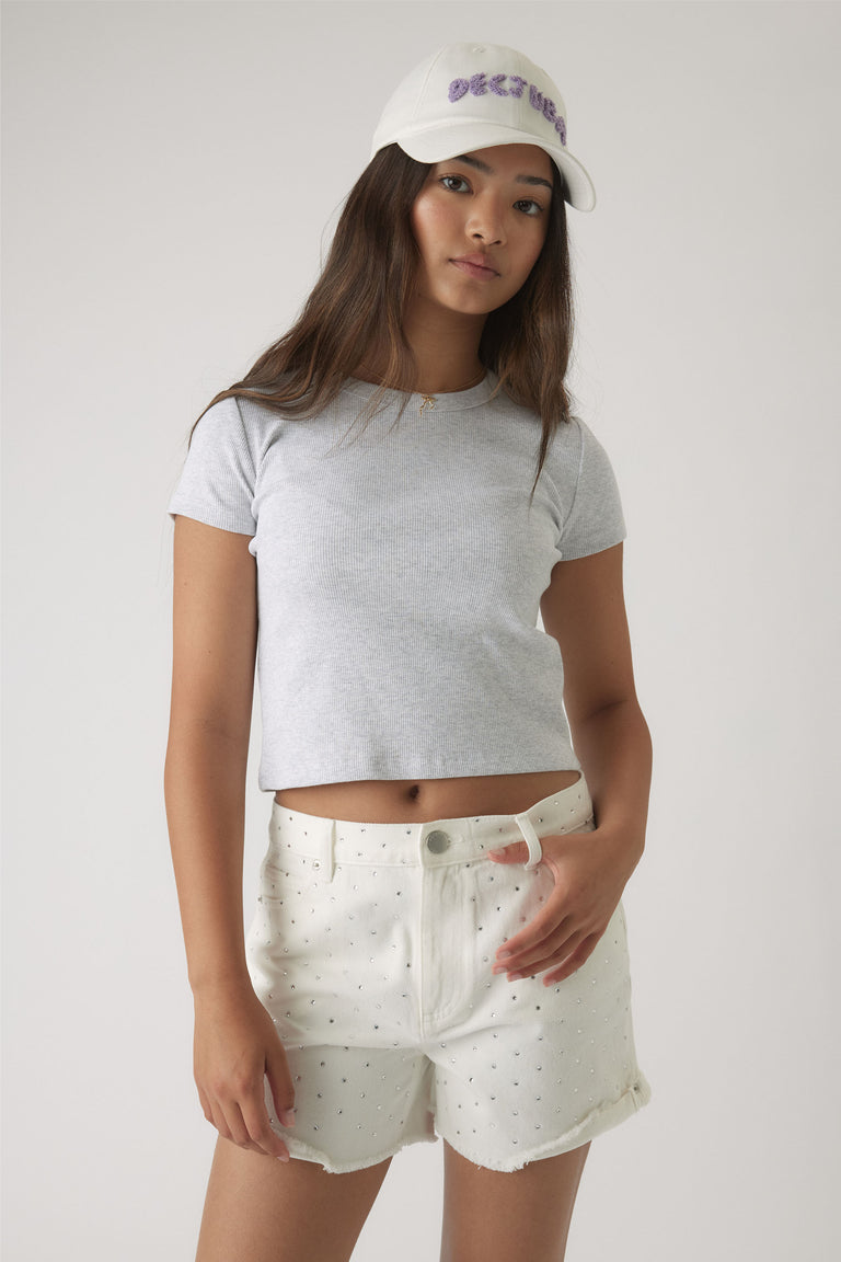 Girl wearing white rhinestone-embellished shorts paired with a light grey cropped tee and white cap.