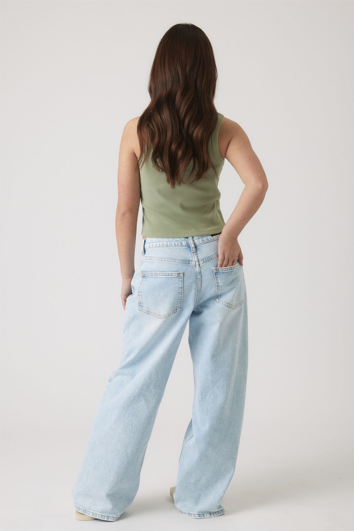 Girl with long hair wearing a sleeveless olive-green tank top paired with relaxed wide-leg light wash denim jeans.
