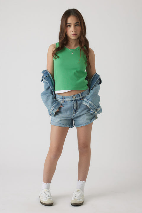 Teen girl wearing a bright green tank top layered over a white tee, paired with rolled-up denim shorts and a denim jacket draped off shoulders