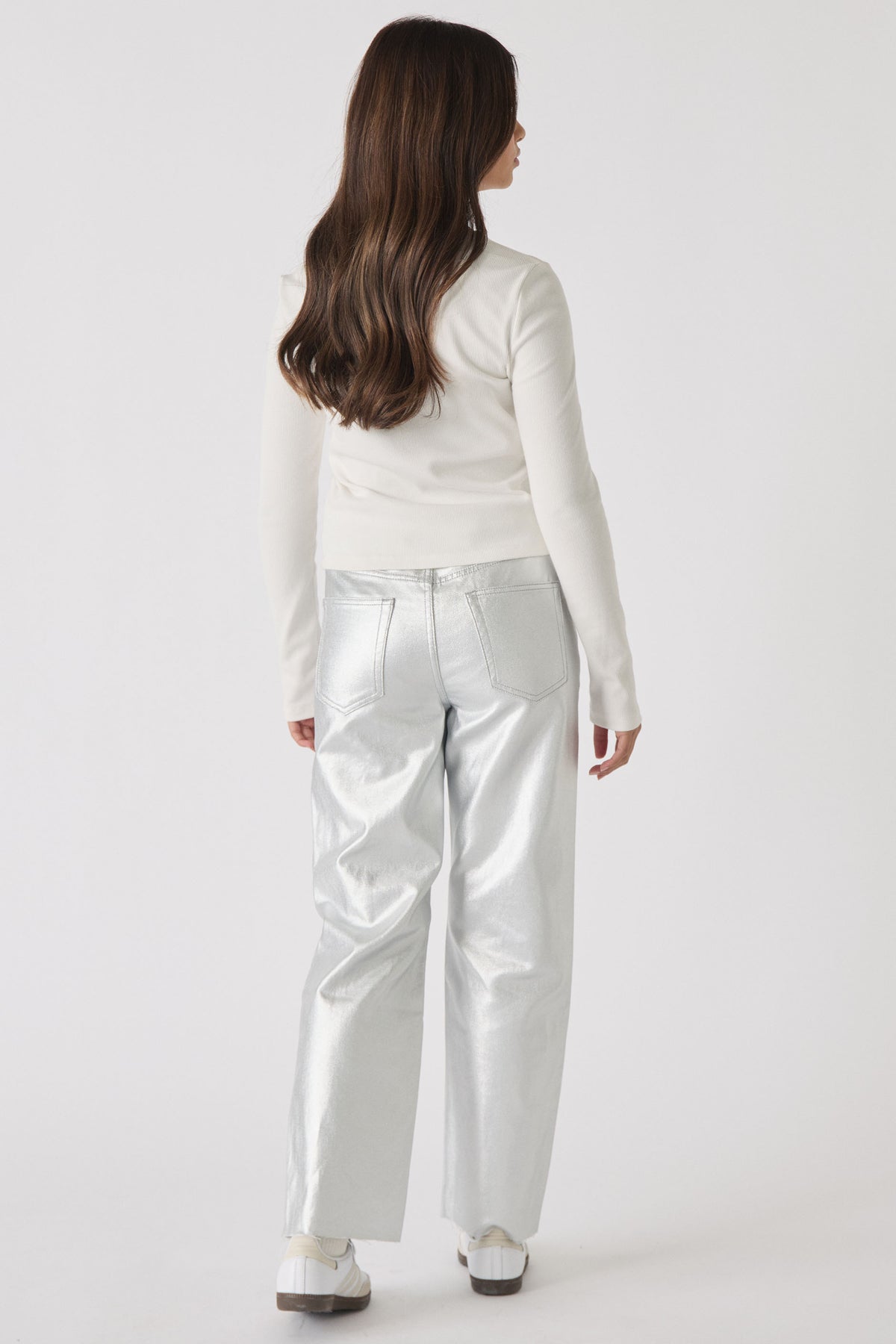 Girl wearing a long-sleeve cream top paired with shiny silver straight-leg jeans and white sneakers, back view