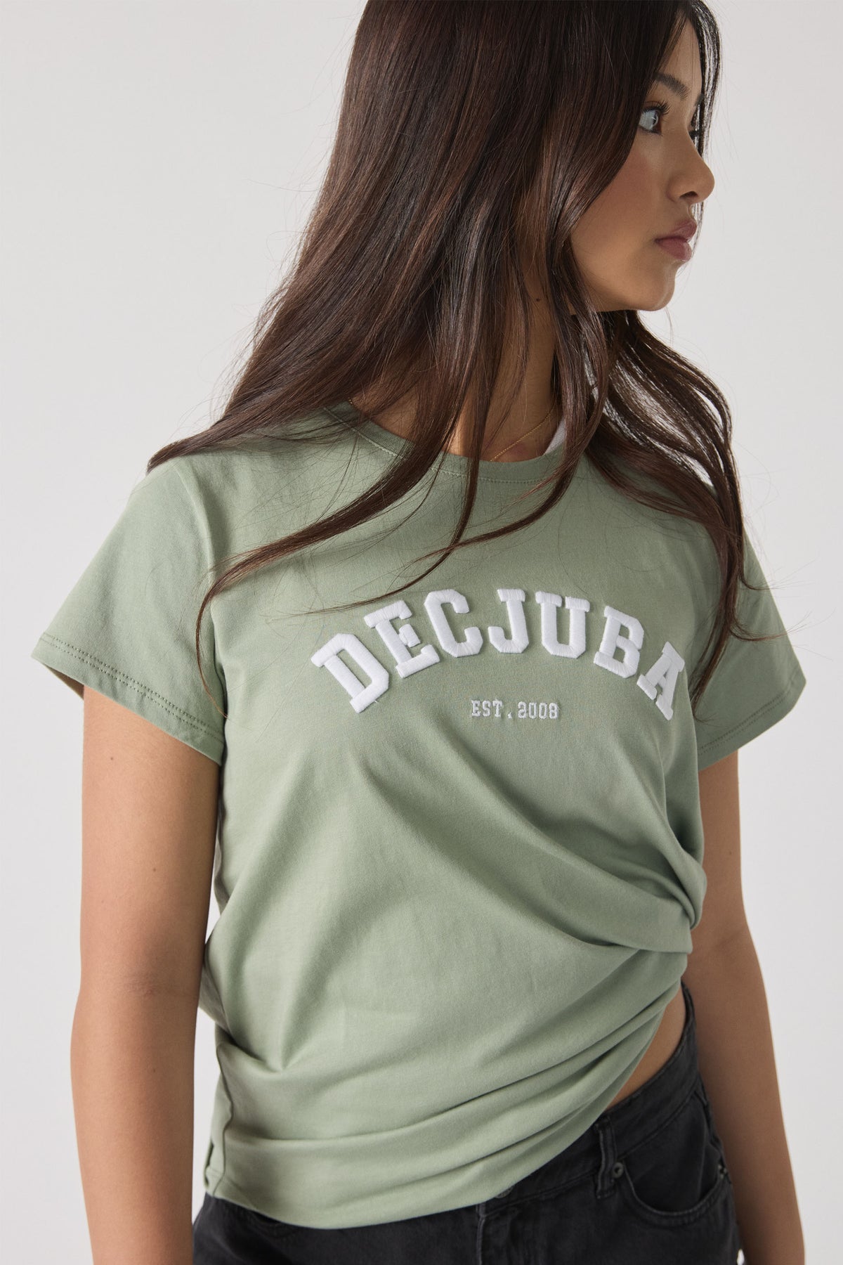 Girl in a soft olive green tee with white text, styled casually with dark denim shorts, looking sideways.
