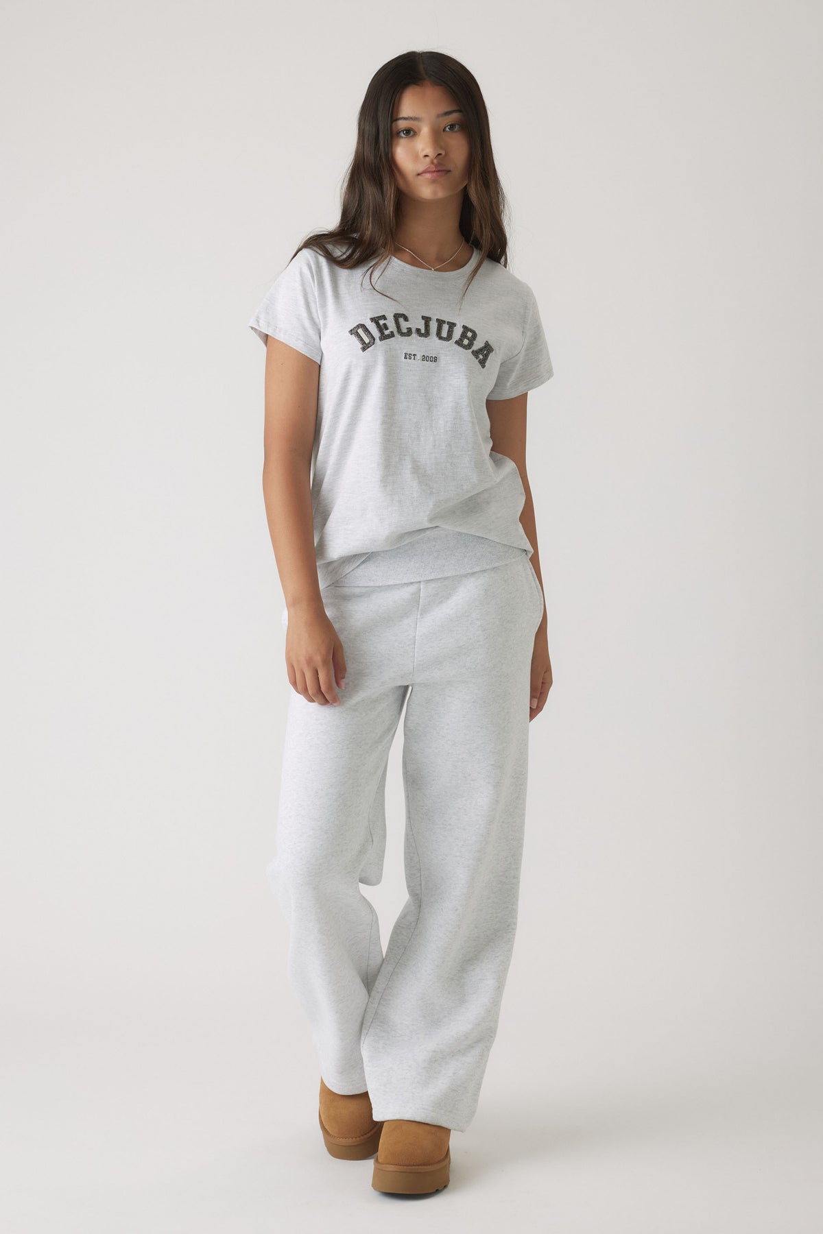 Girl wearing a light grey casual tee with logo text paired with matching relaxed sweatpants and tan slip-on boots