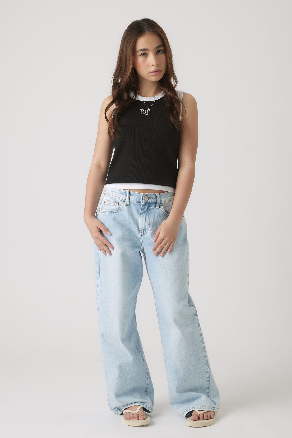 Teen girl wearing a black and white sleeveless tank paired with light-wash wide-leg jeans and sandals for casual style