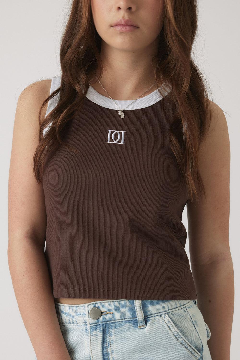 Girl wearing a chocolate brown ribbed tank with white trim and a monogram detail, paired with light wash denim shorts.