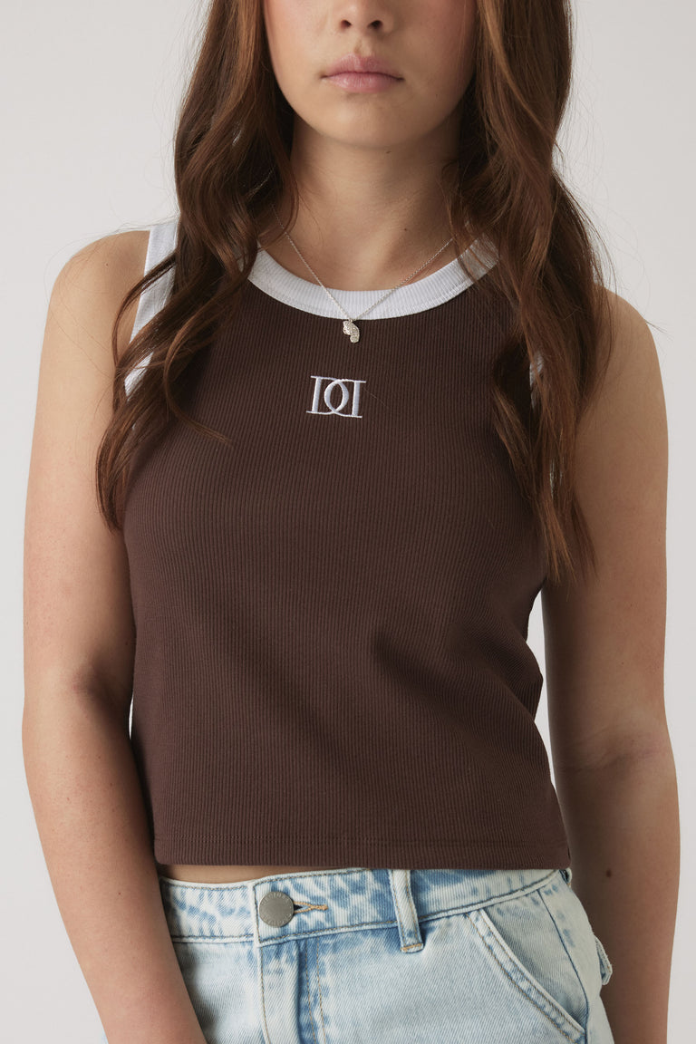 Girl wearing a chocolate brown ribbed tank with white trim and a monogram detail, paired with light wash denim shorts.