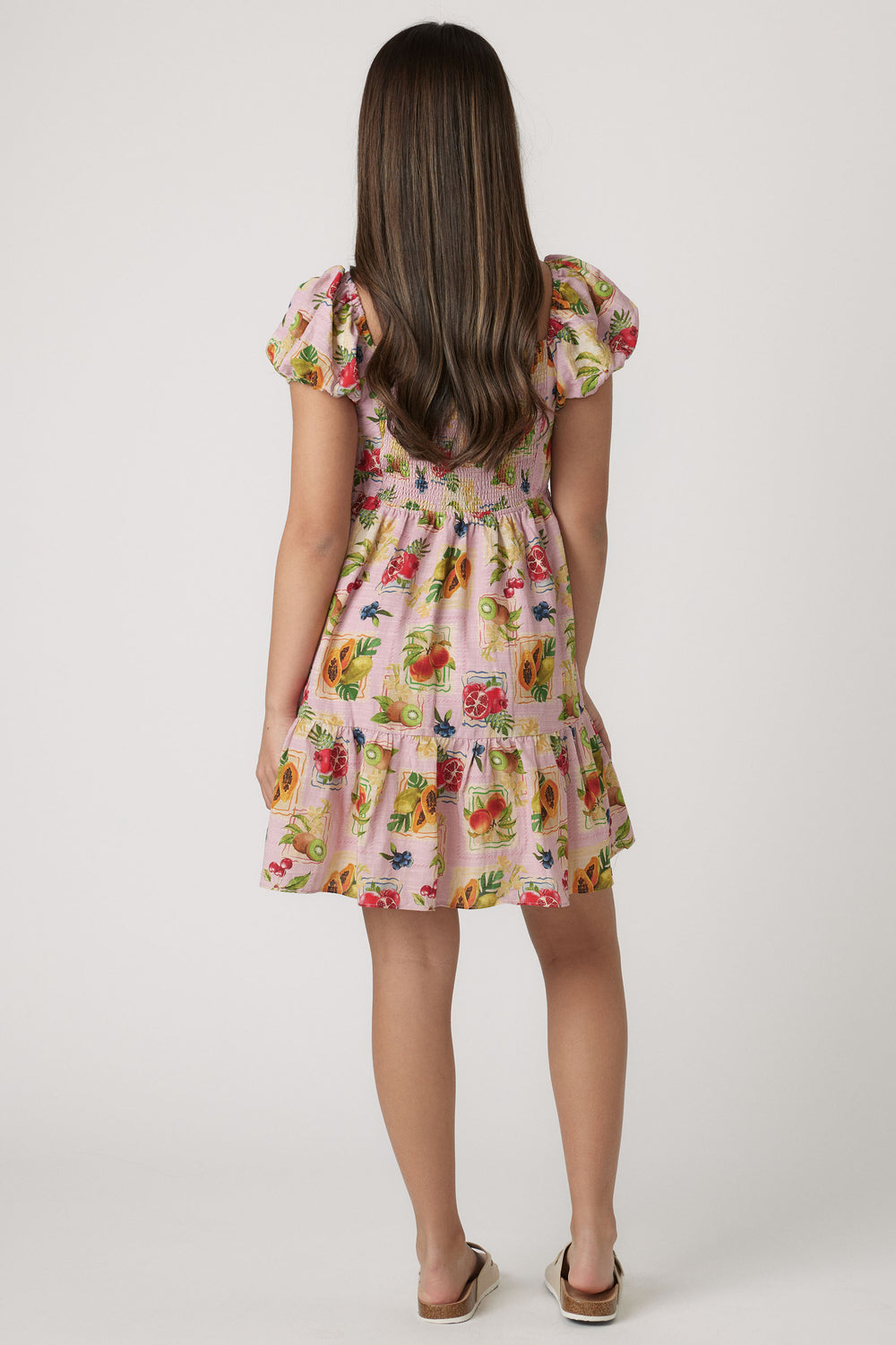 Young girl wearing a pink mini dress with puff sleeves and colorful fruit print, styled for casual wear