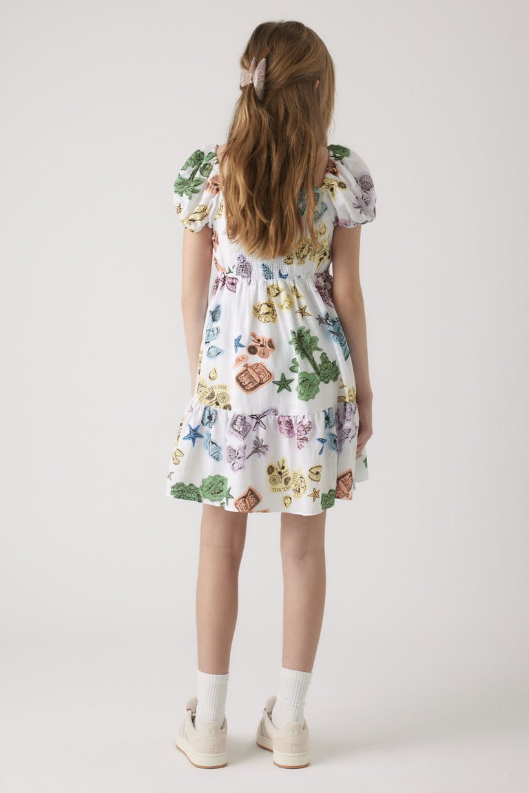 Girl wearing a white mini dress with colorful nature-inspired prints and puff sleeves, paired with white socks and sneakers.